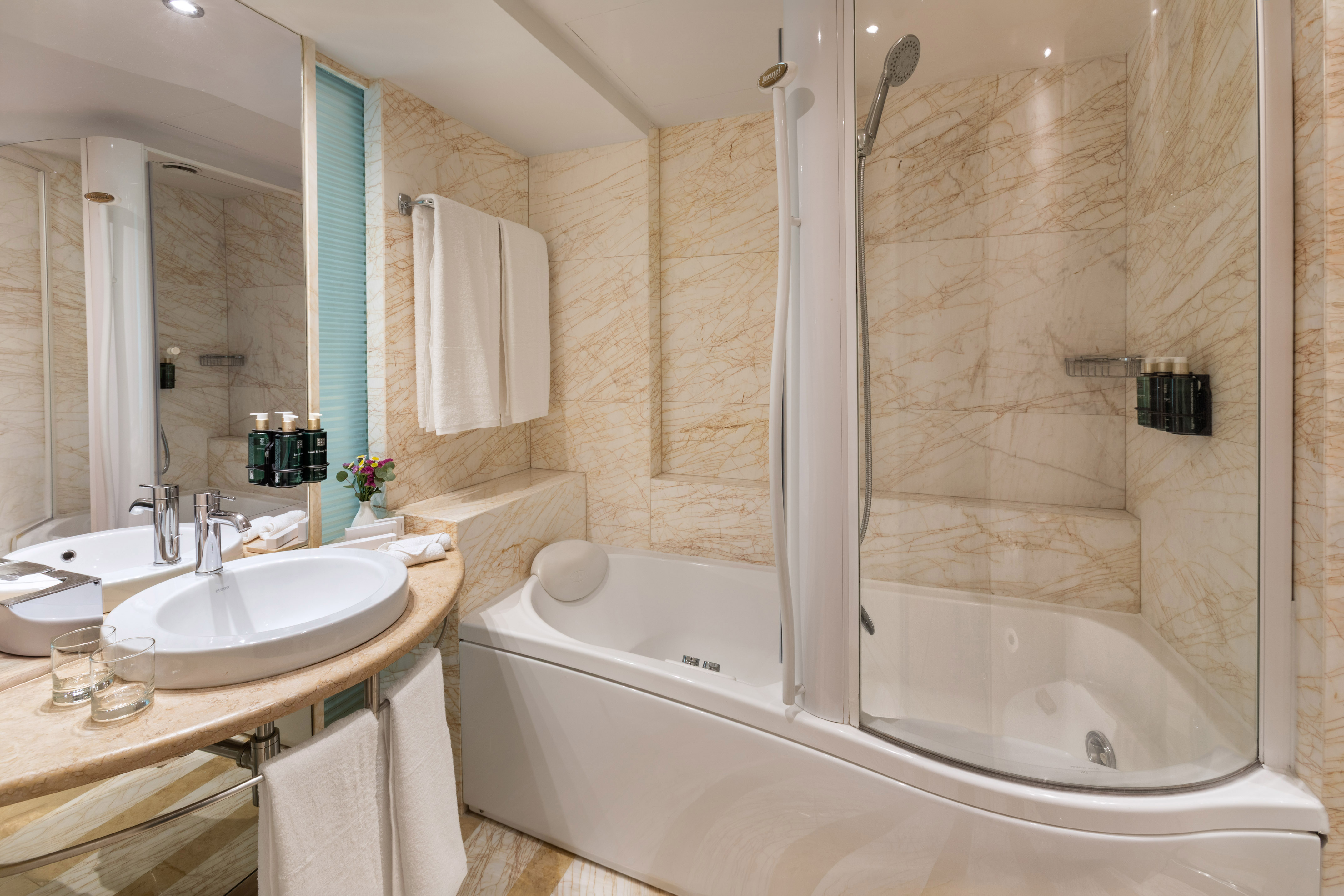 Luxury hotel bathroom with marble walls, bathtub, shower, and sink.