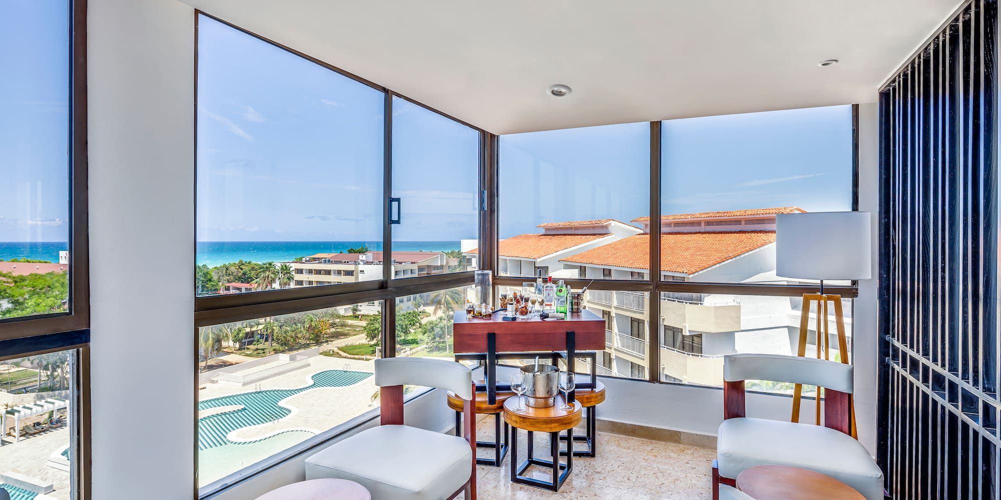 a room with a table and chairs and a pool overlooking the ocean