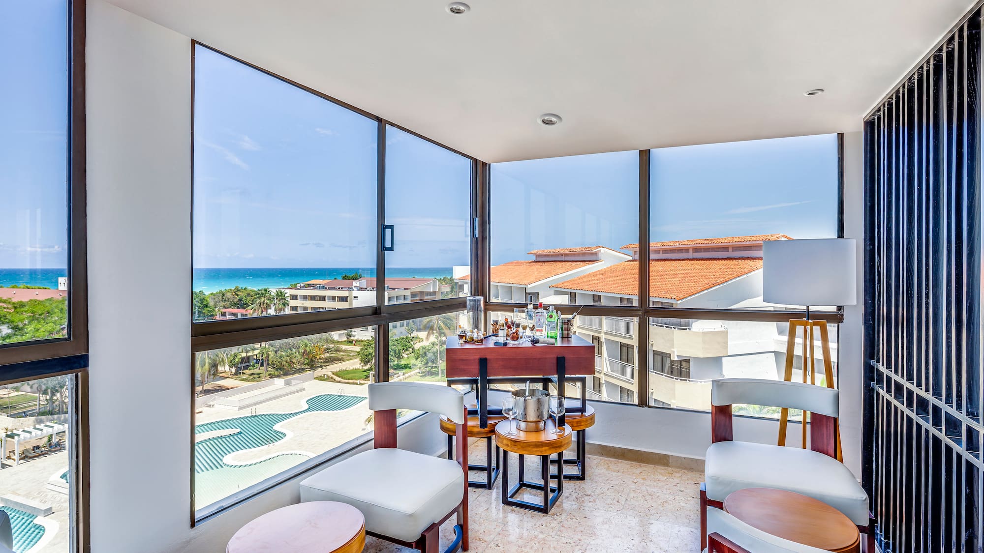 a room with a table and chairs and a pool overlooking the ocean