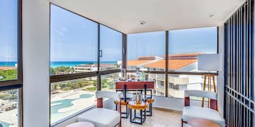 a room with a table and chairs and a pool overlooking the ocean