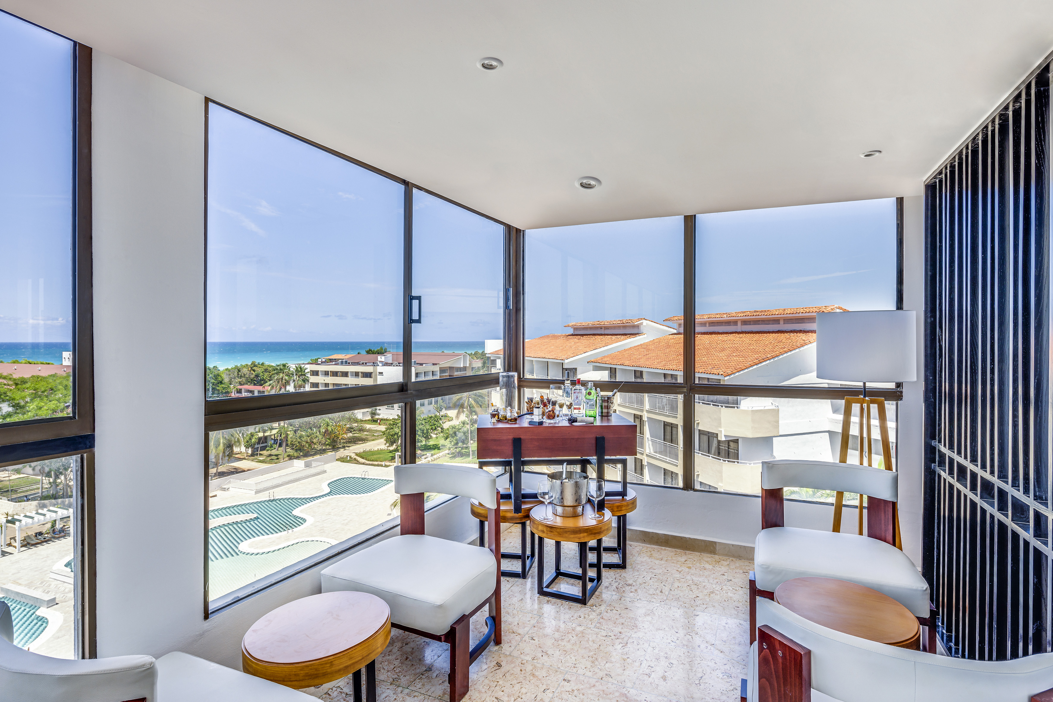 a room with a table and chairs and a pool overlooking the ocean