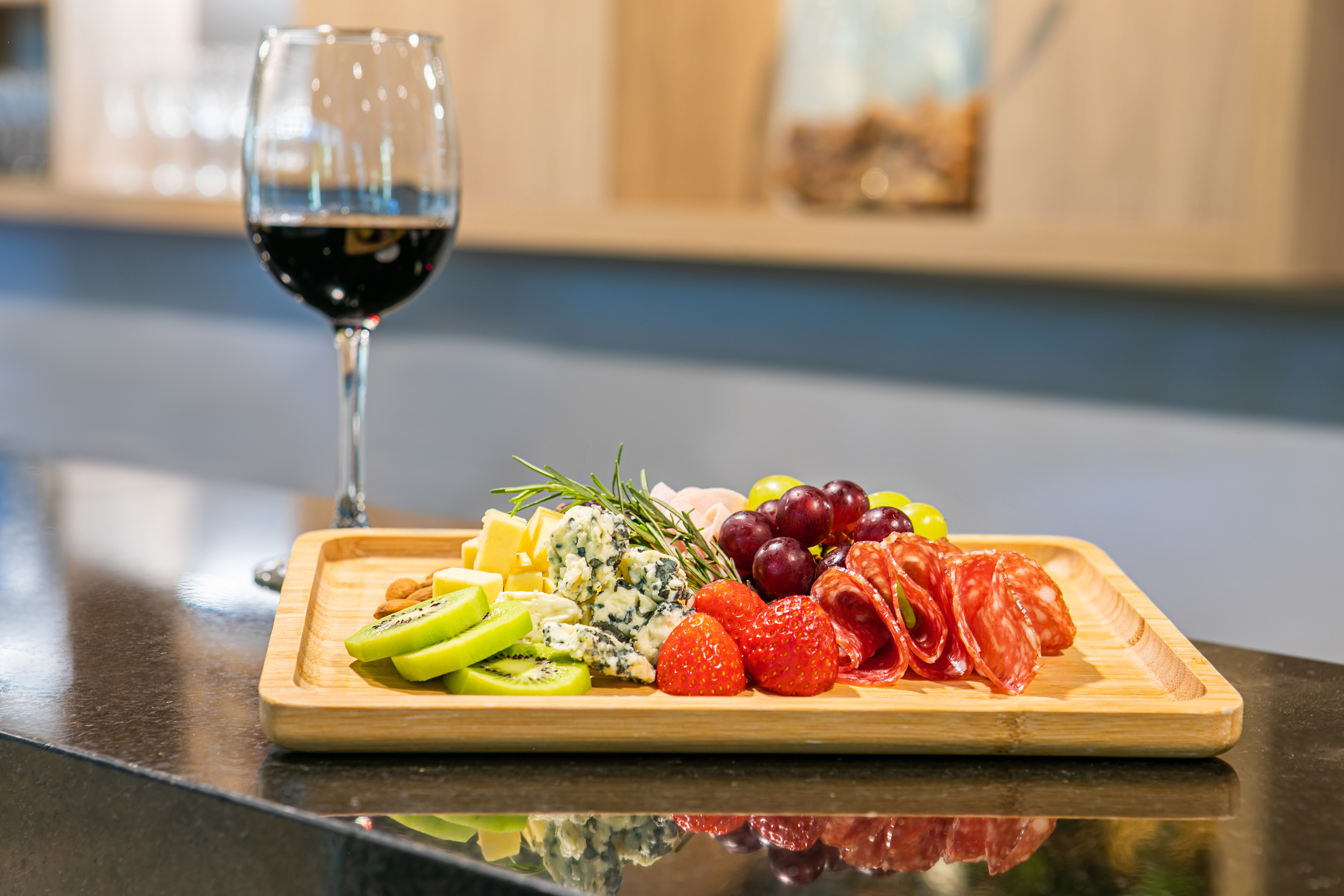 Gourmet charcuterie board with cheese, salami, grapes, kiwi, and red wine.