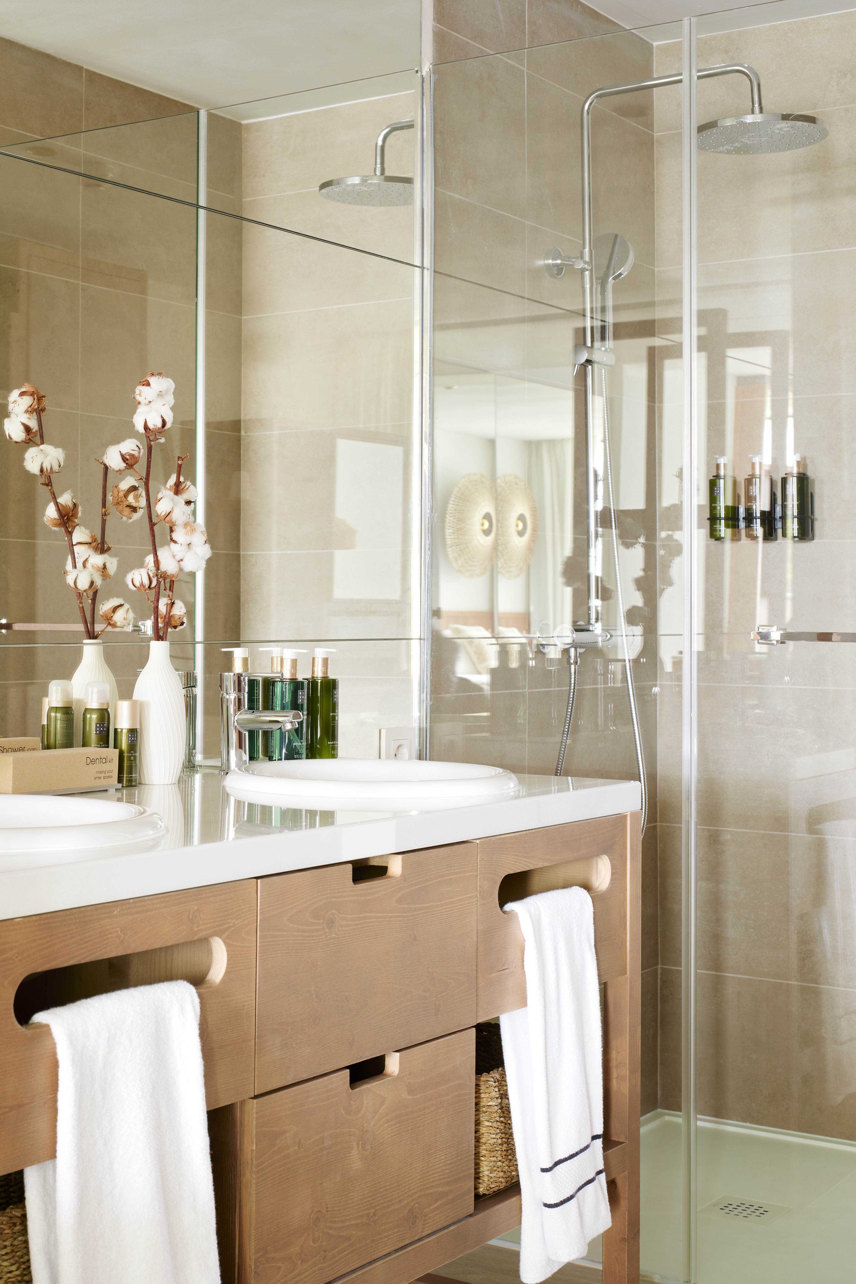 Modern bathroom with double wooden vanity, glass shower, and beige tiles.