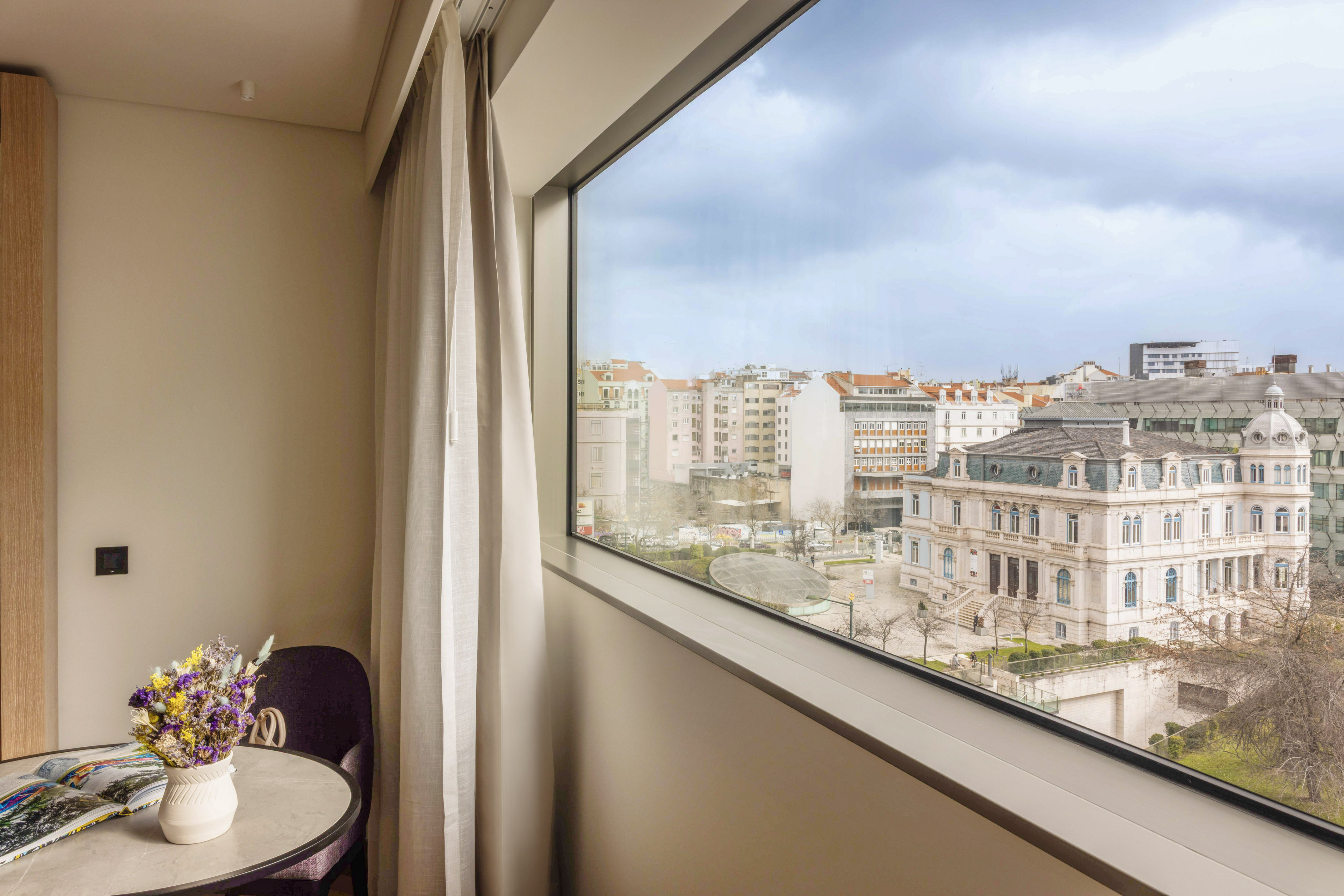 Modern hotel room with large window city view, historic building.