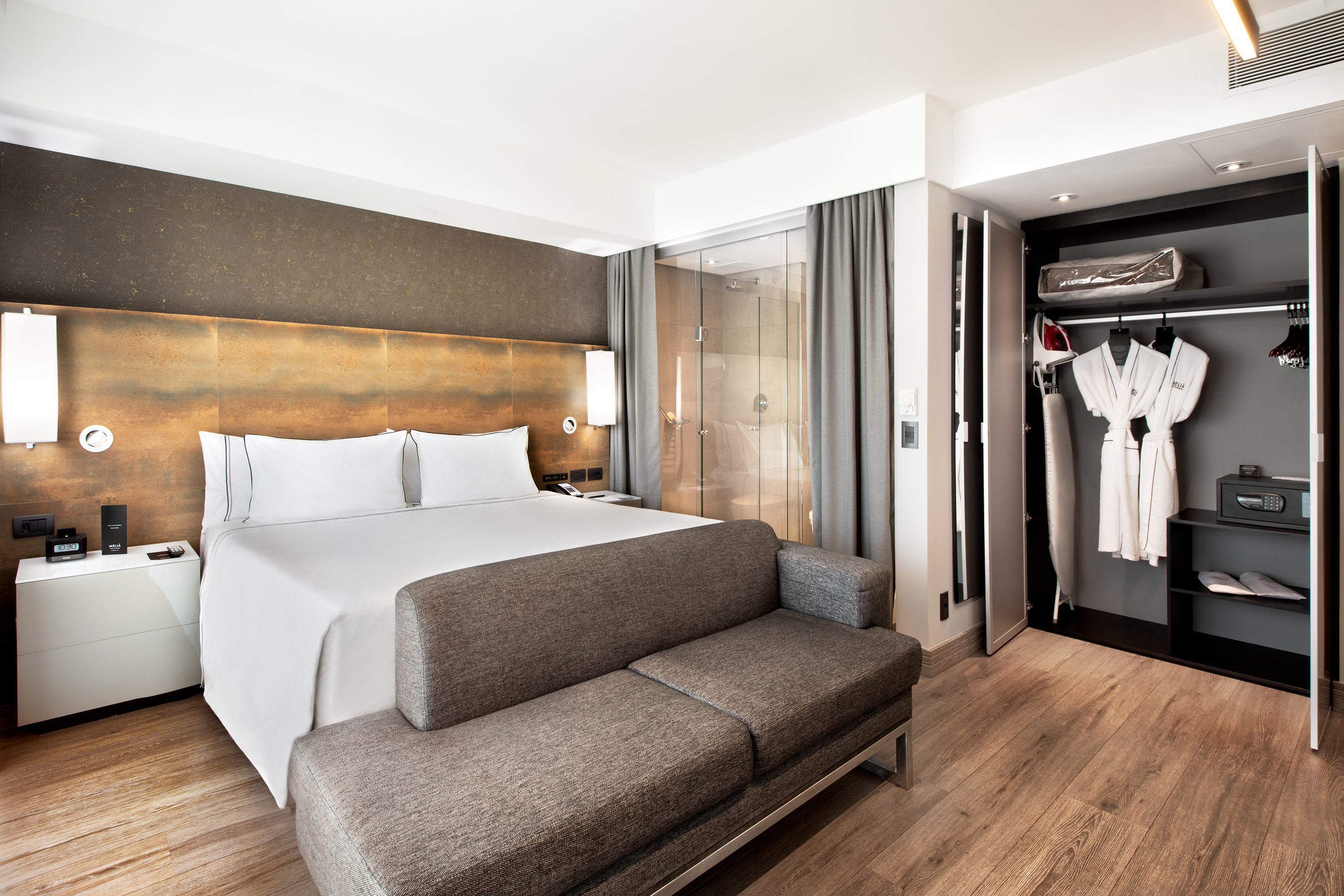 Modern hotel room with bed, sofa, glass shower, and closet with robes & iron.