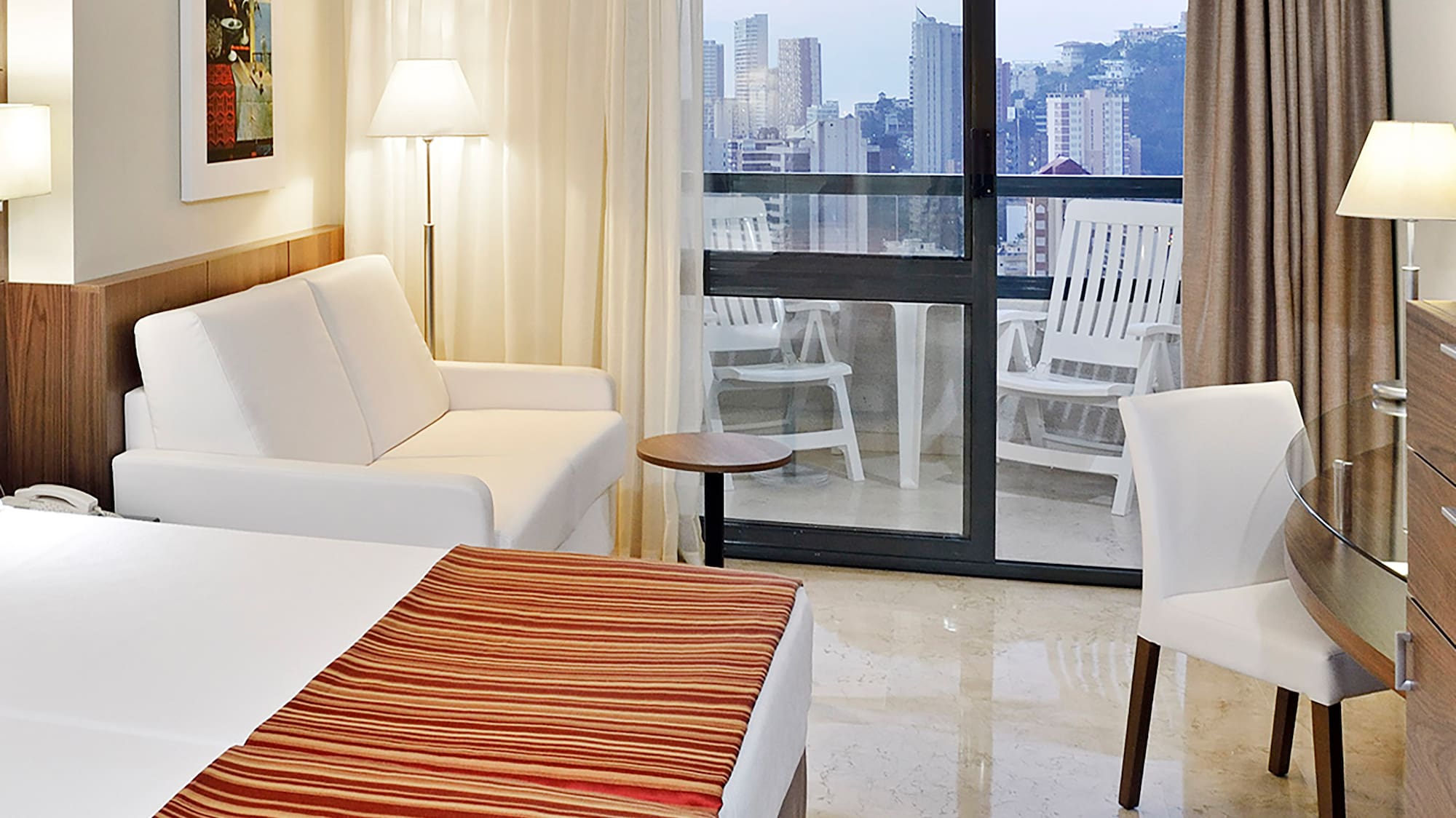 a hotel room with a bed and chairs and a glass door