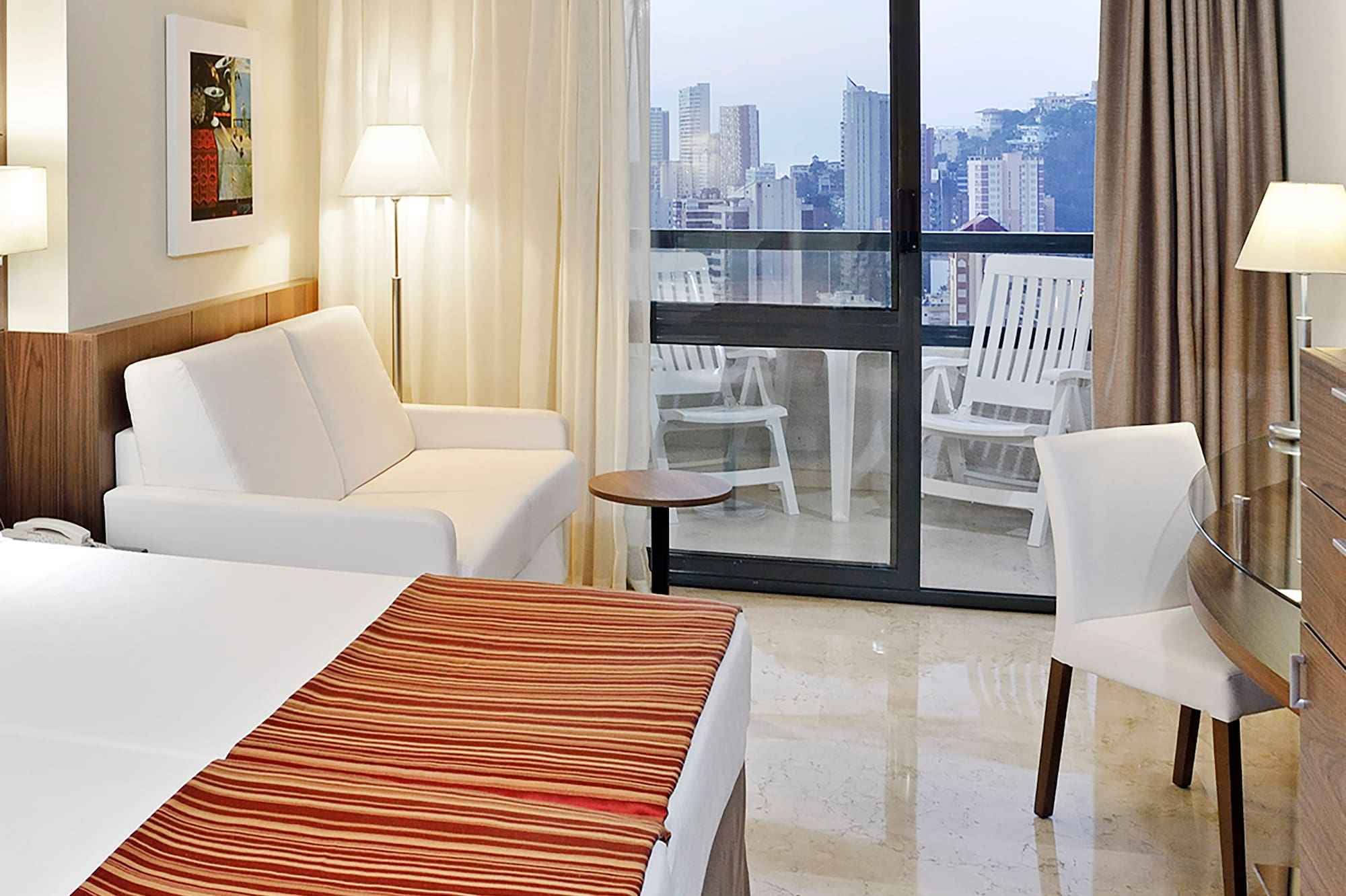 a hotel room with a bed and chairs and a glass door
