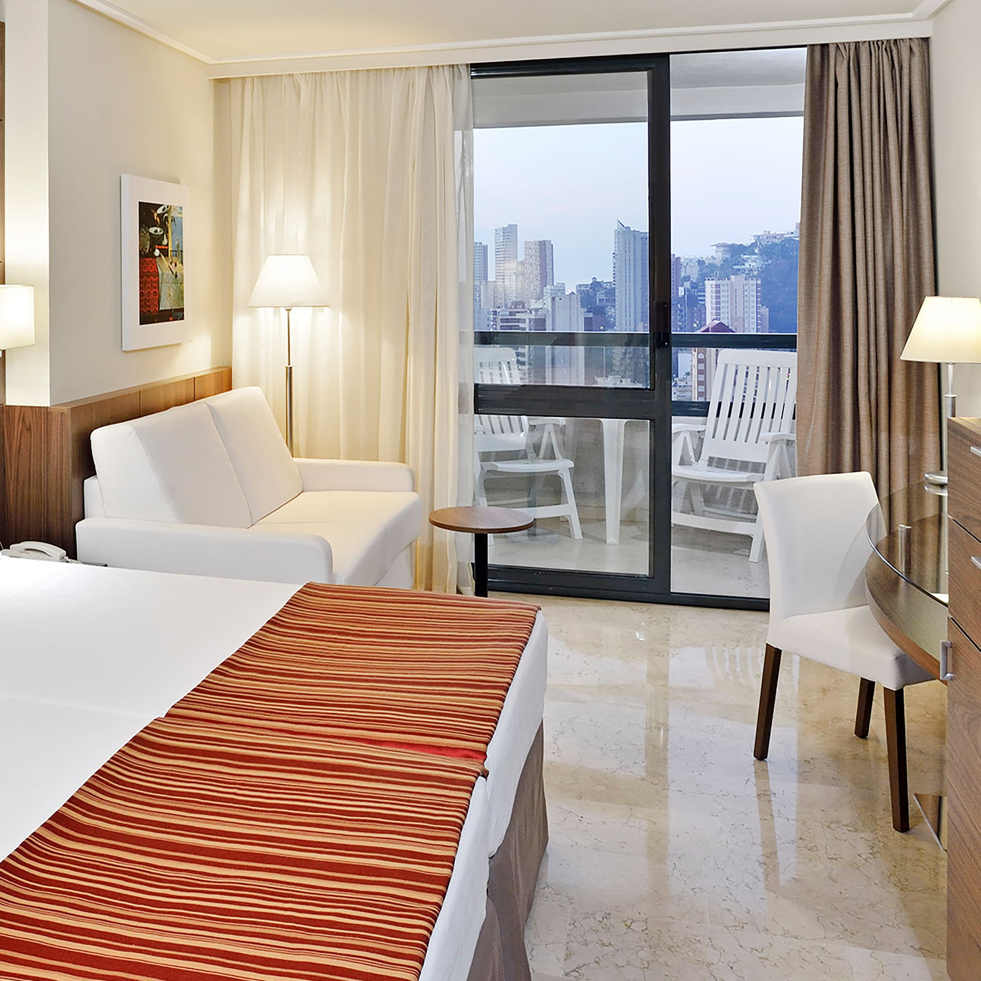 a hotel room with a bed and chairs and a glass door