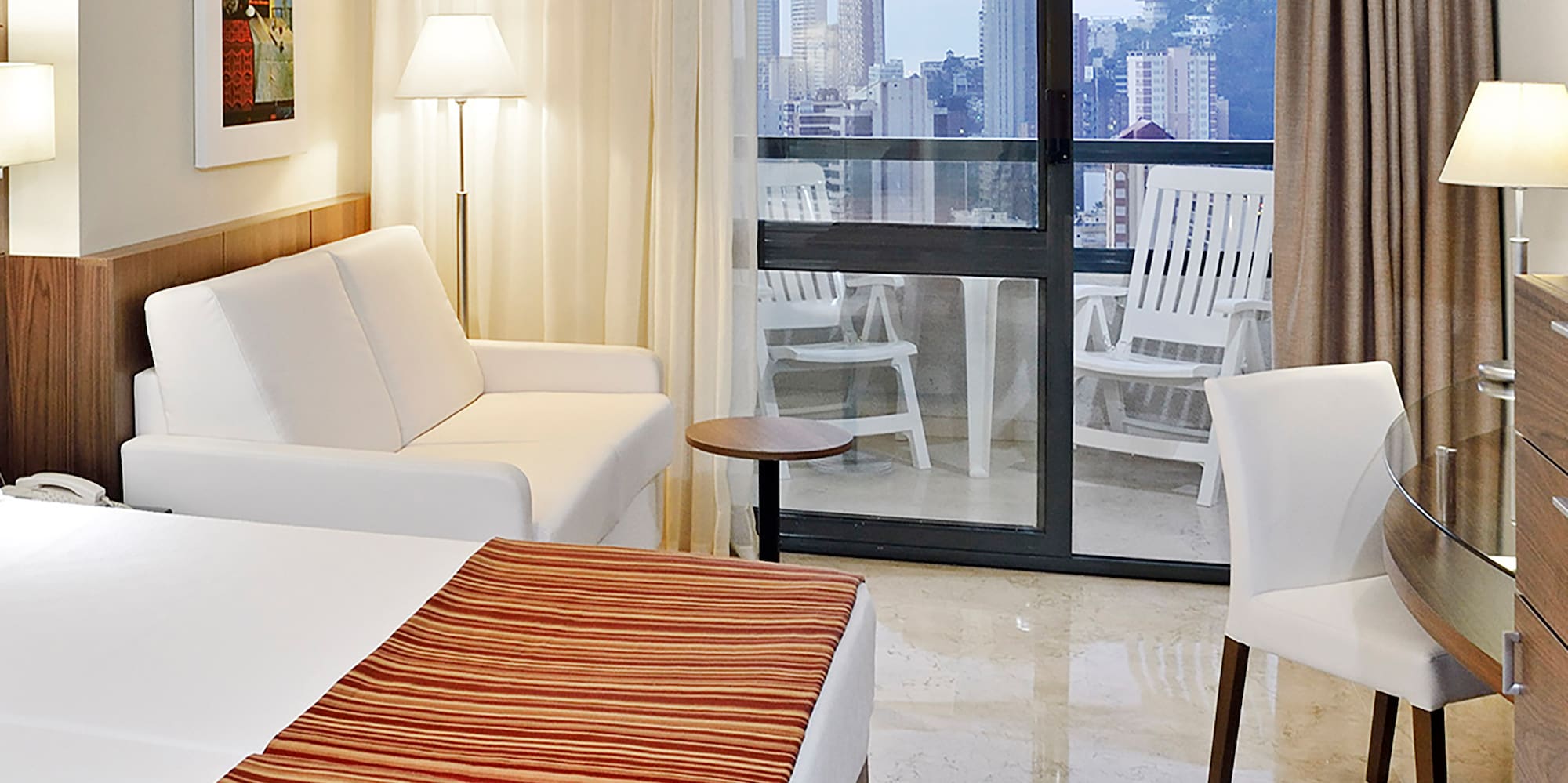 a hotel room with a bed and chairs and a glass door