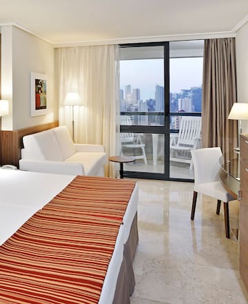a hotel room with a bed and chairs and a glass door