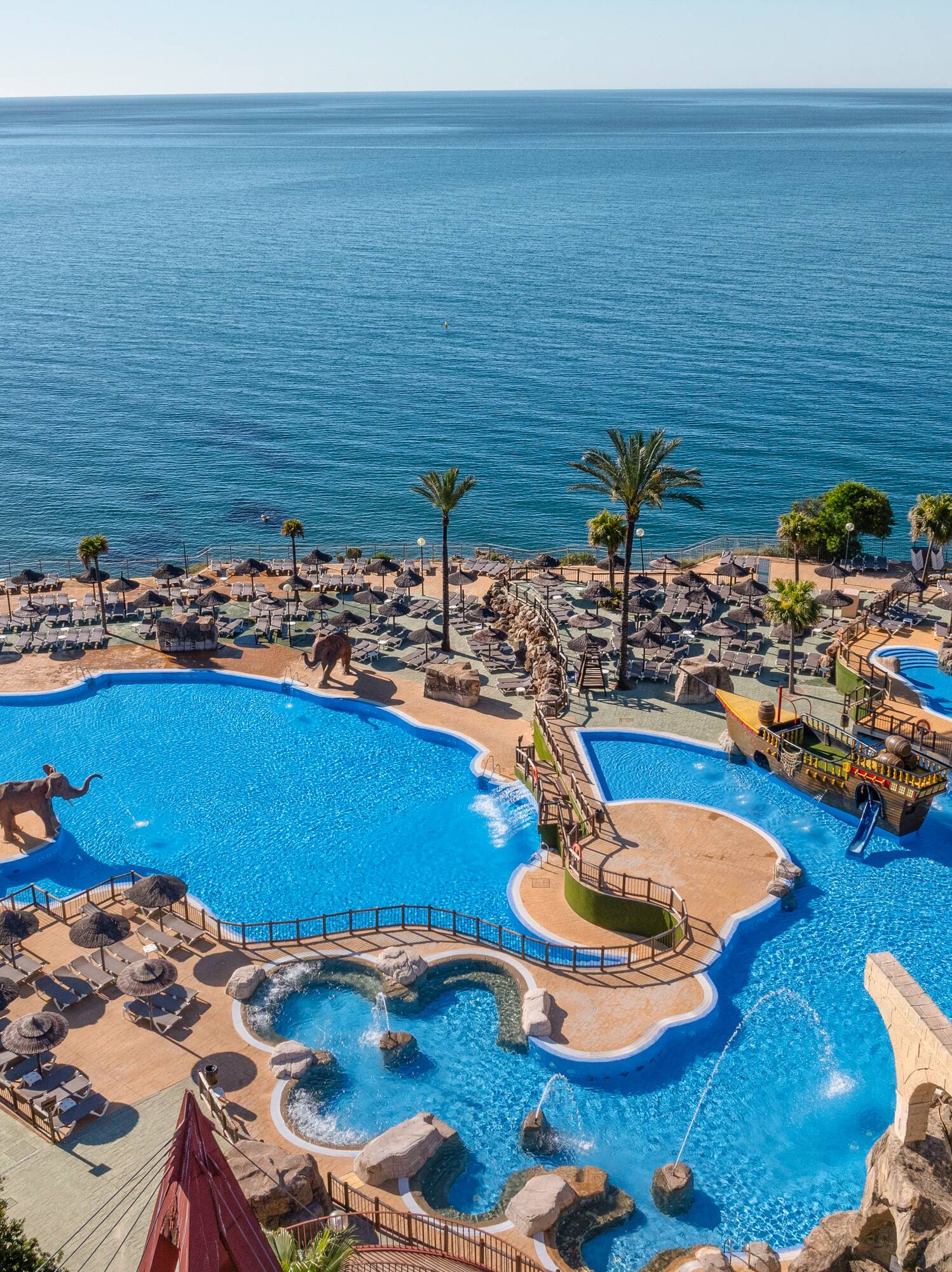 Oceanfront resort pool with water slides, elephant figures, and palm trees.
