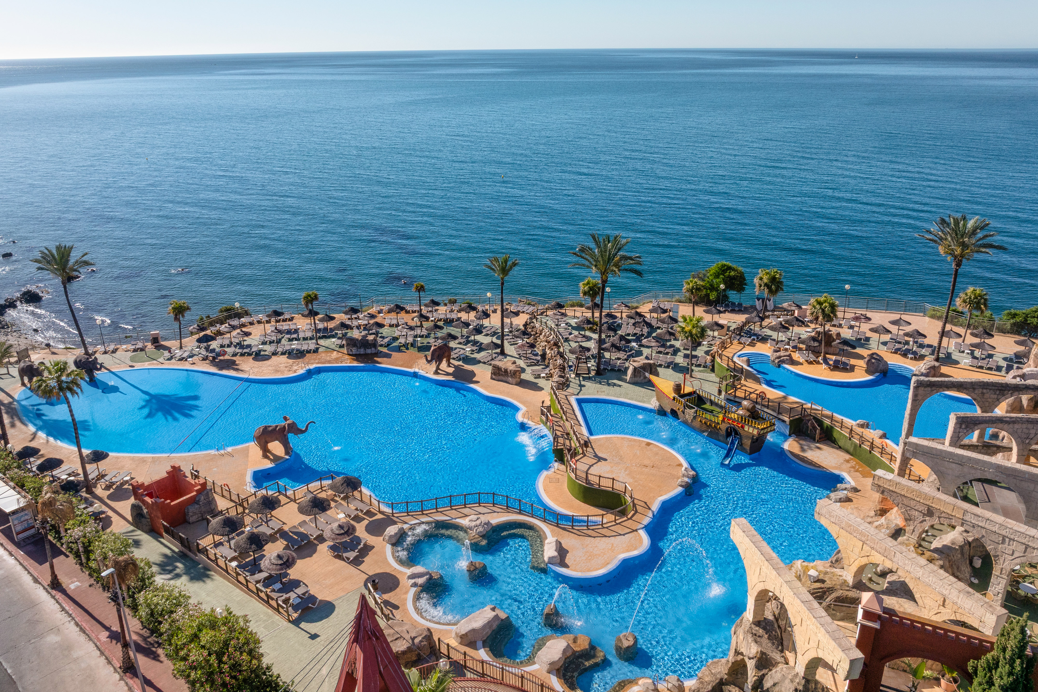 Oceanfront resort water park with pools, palm trees, and sun loungers.
