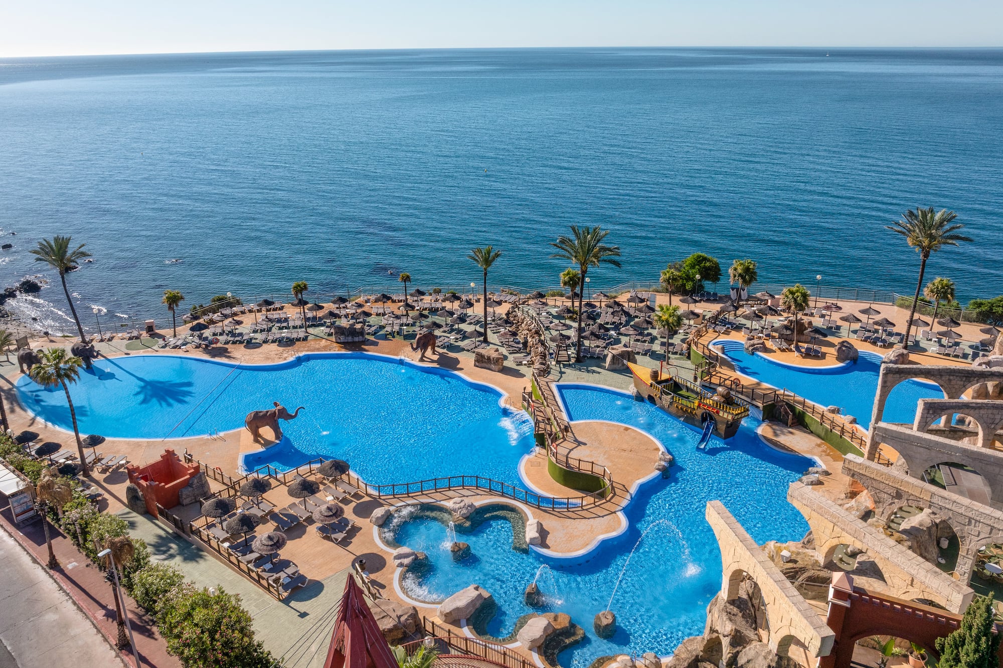 Oceanfront resort water park with pools, palm trees, and sun loungers.