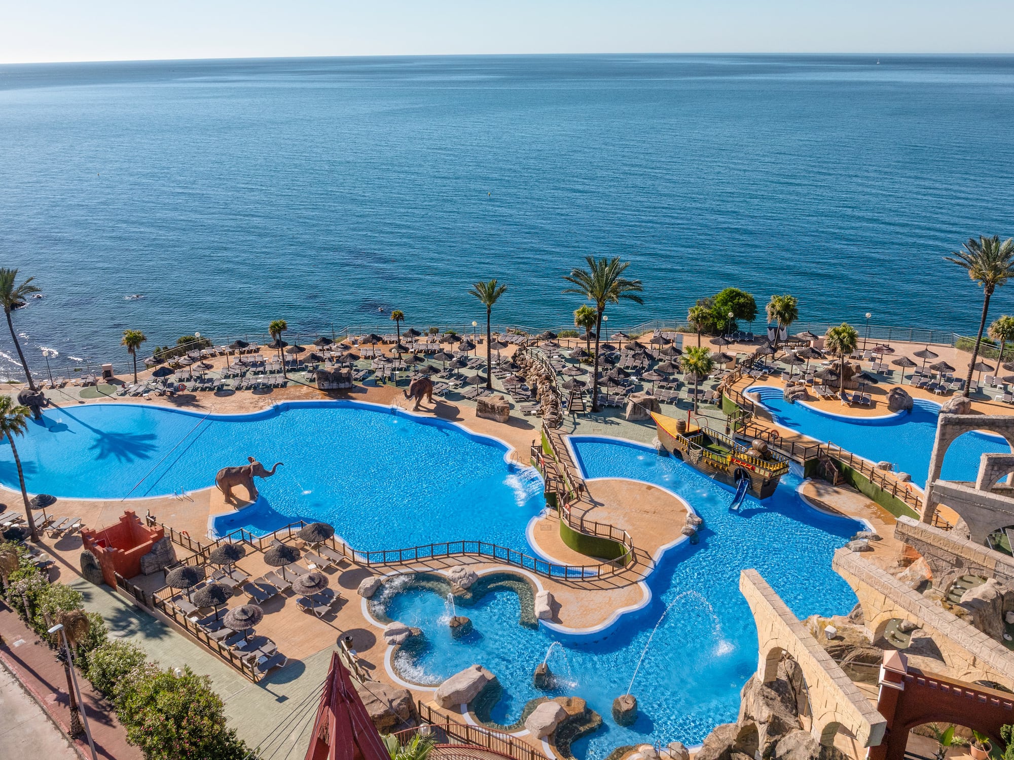 Tropical resort water park, pools, elephant statues, ocean view.