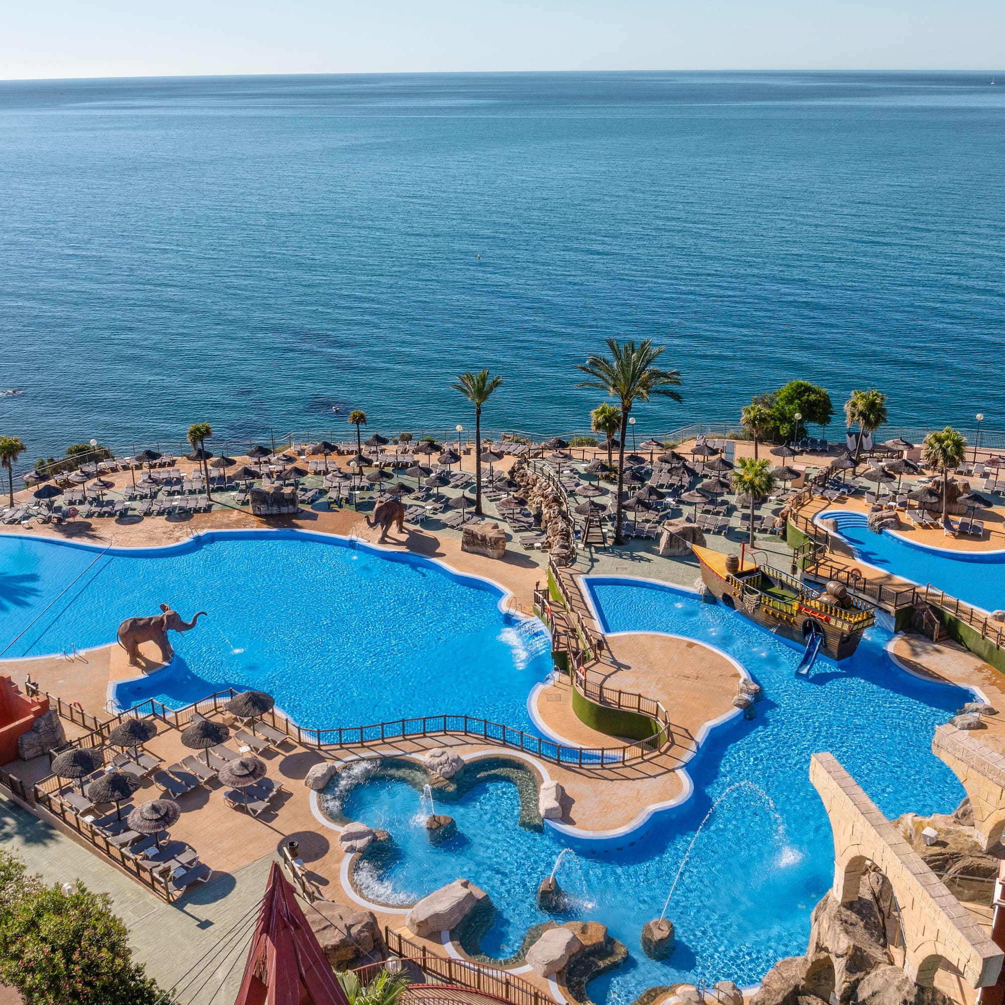 Tropical resort water park overlooking the sea with pools and palm trees.