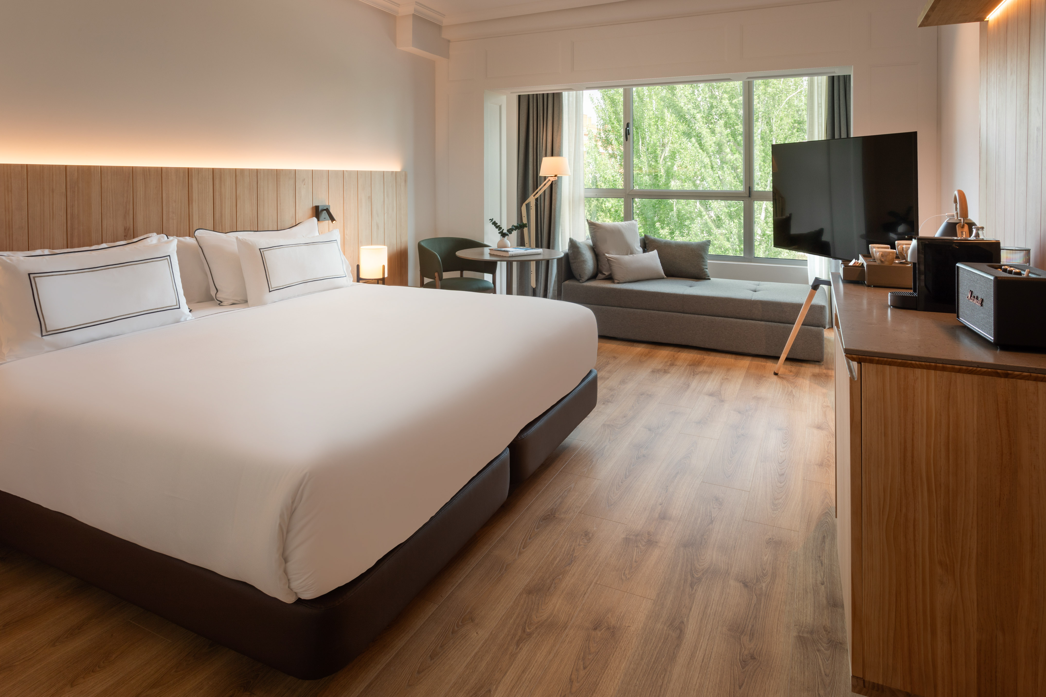 Modern hotel bedroom with large bed, window seating, TV, and hardwood floor.