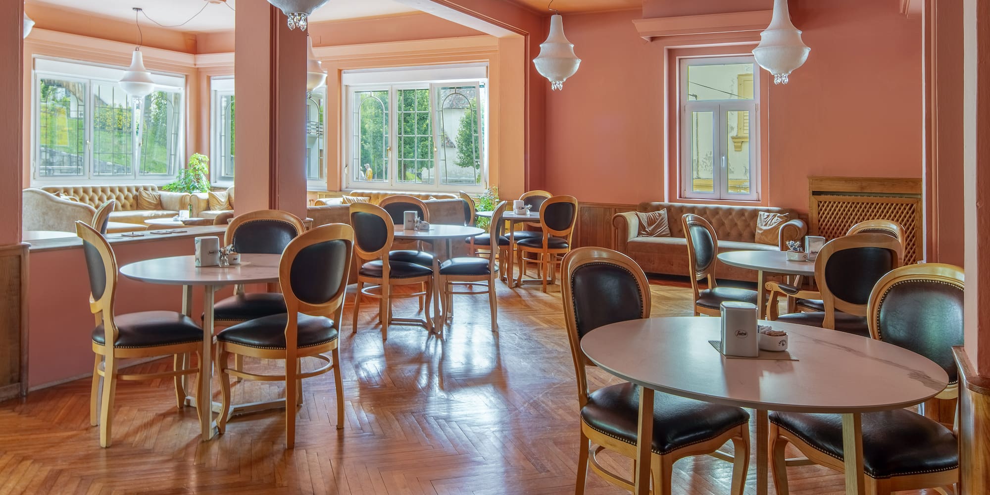 Peach-toned restaurant lounge with round tables, dark chairs, wood floor.