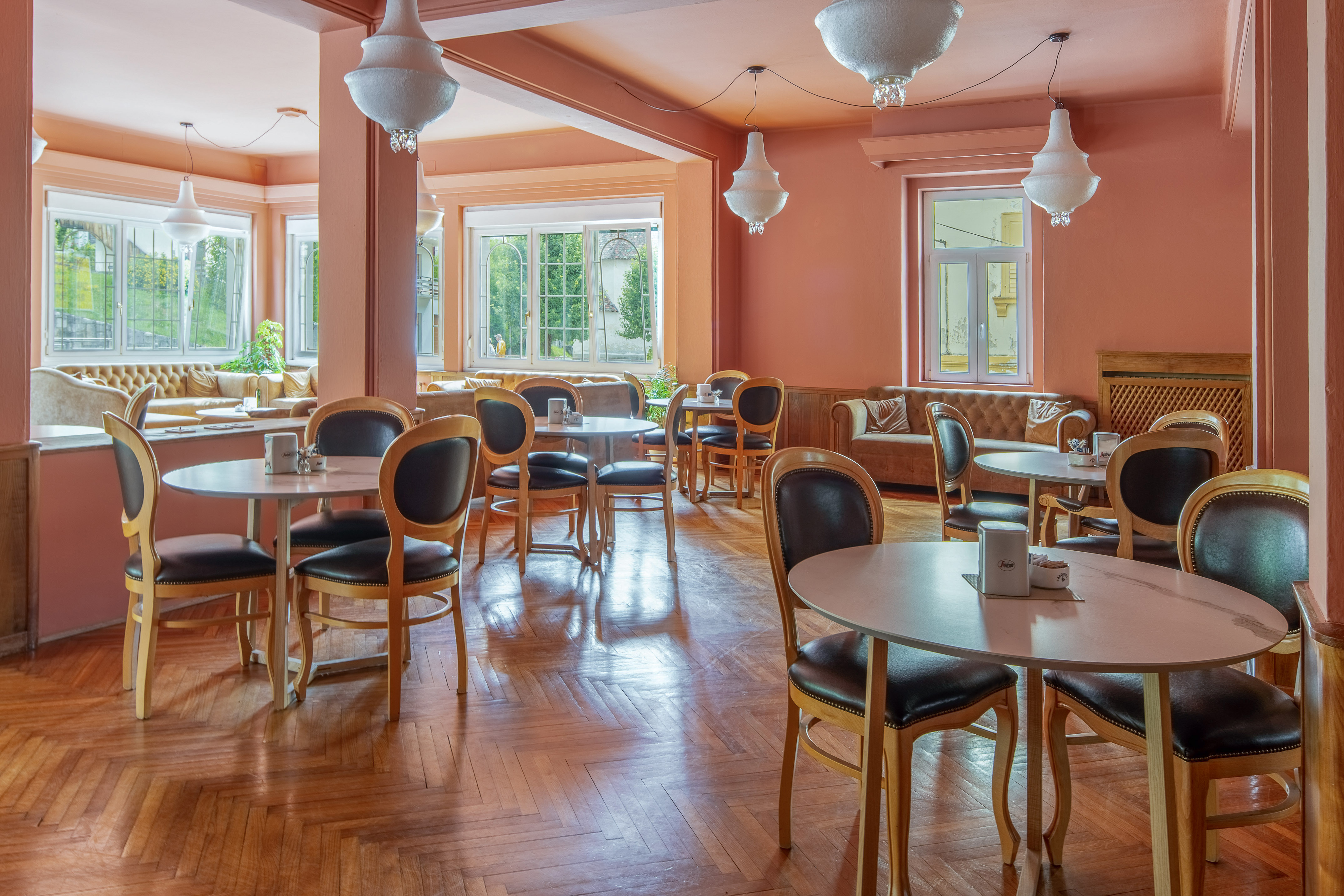 Peach-toned restaurant lounge with round tables, dark chairs, wood floor.