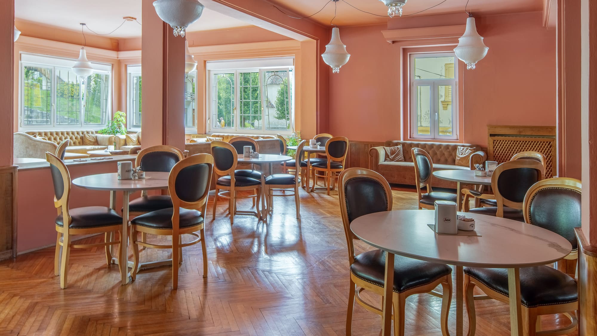 Peach-toned restaurant lounge with round tables, dark chairs, wood floor.