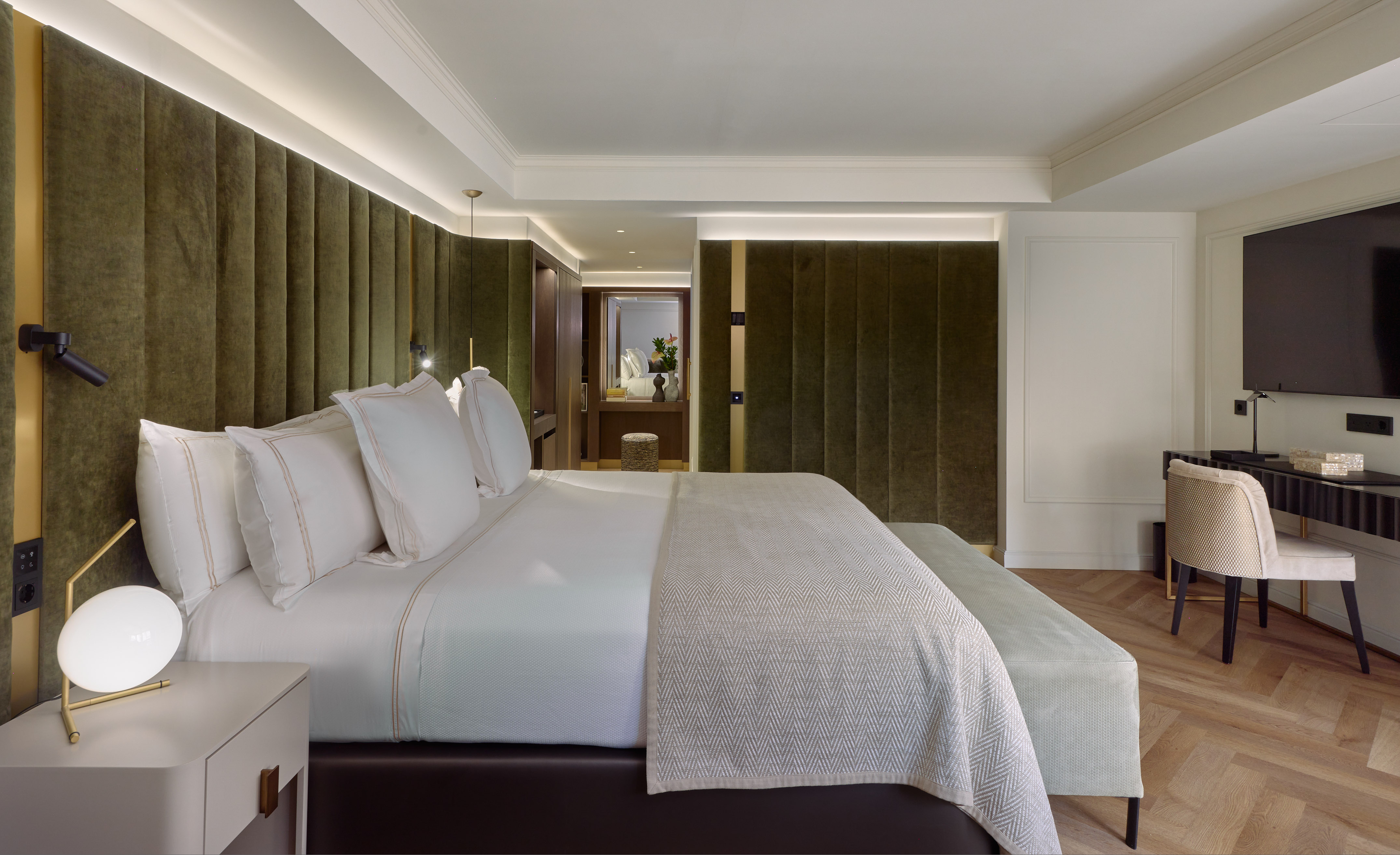 Luxury hotel bedroom with green velvet wall, white bed, and modern furnishings.