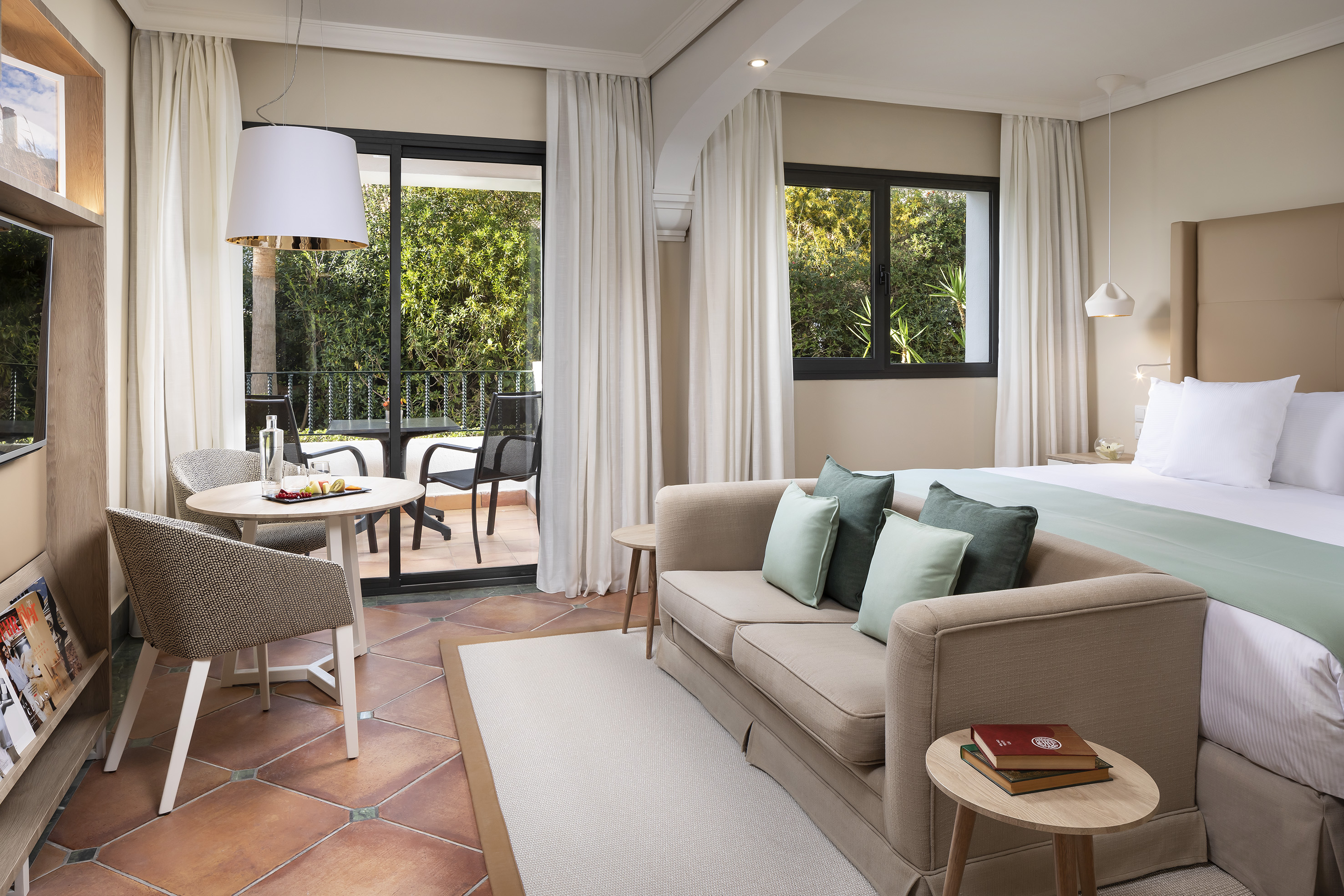 Spacious hotel suite with balcony, king bed, and lounge area with sofa.