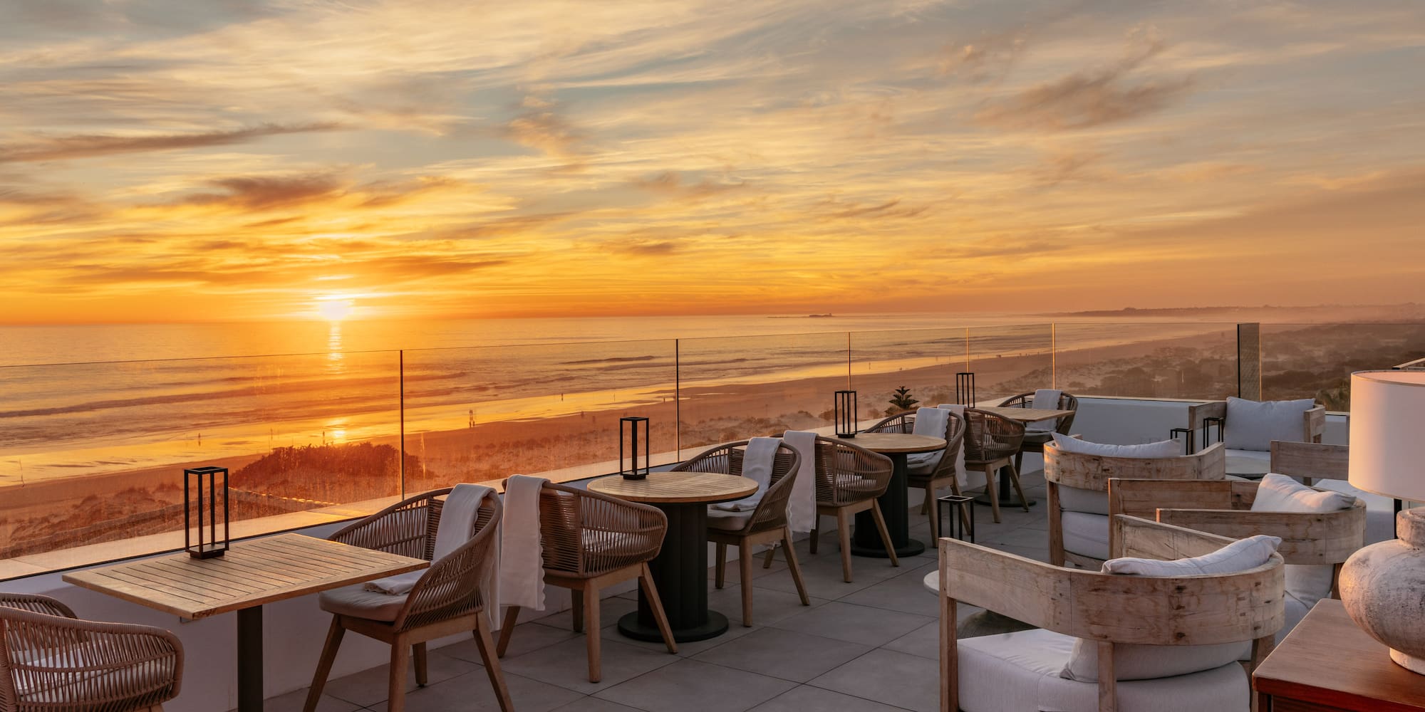 Rooftop terrace with ocean sunset view, outdoor dining tables and beach.