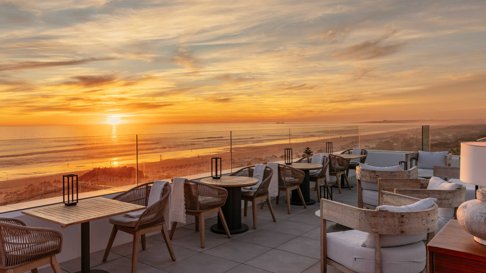 Rooftop dining terrace overlooking ocean and beach at golden sunset.