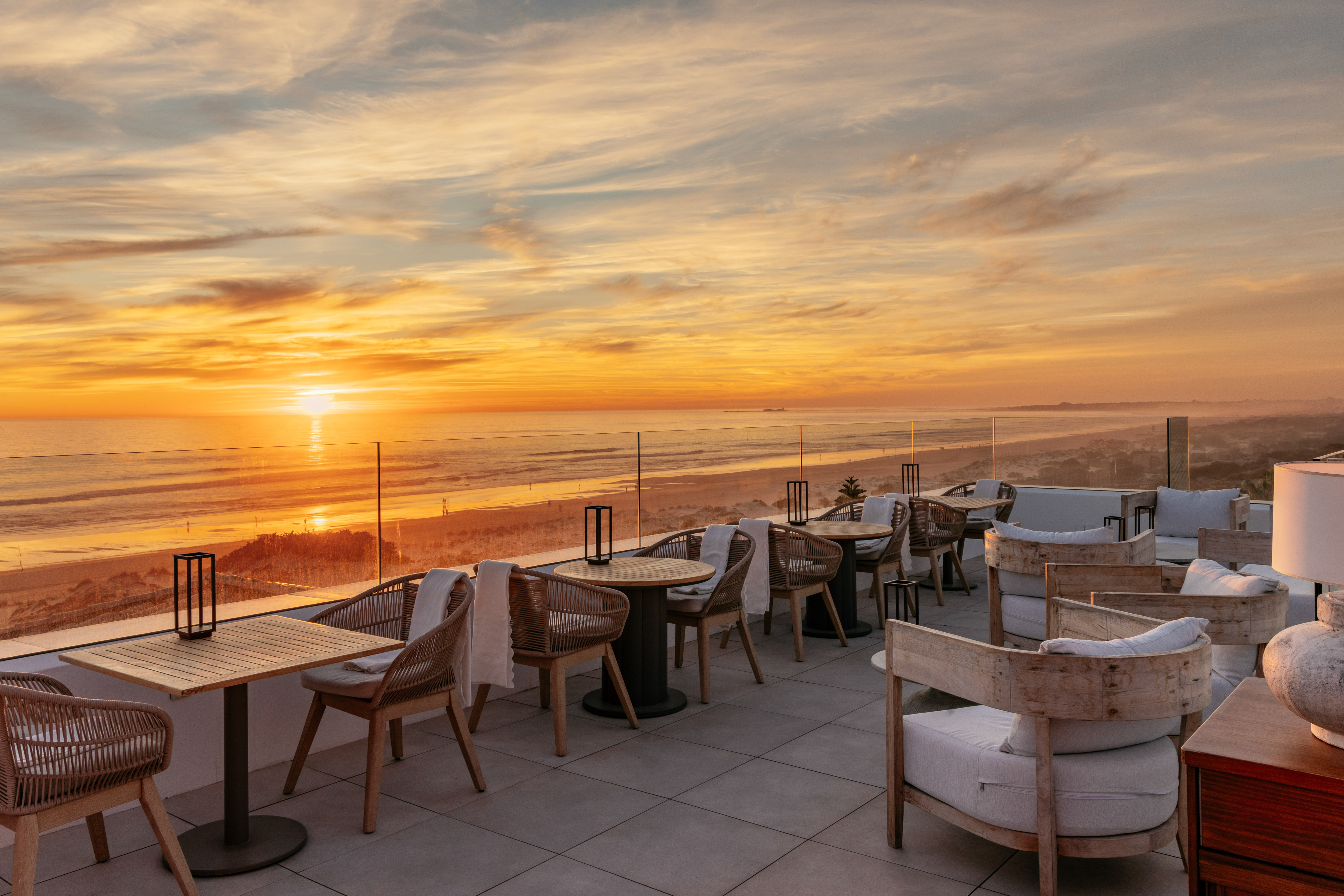 Rooftop dining terrace overlooking ocean and beach at golden sunset.
