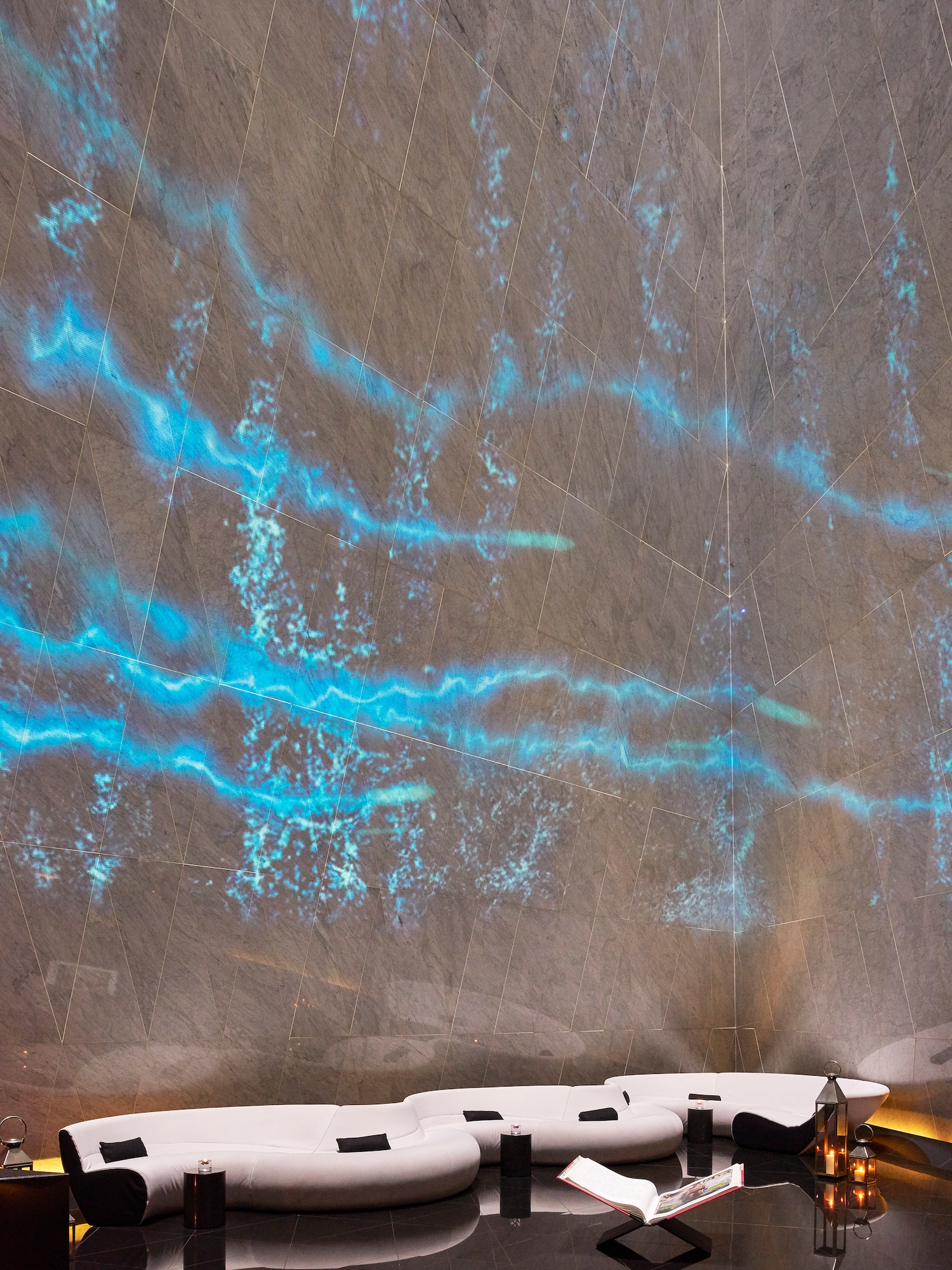 Luxury lounge with blue light wall art, white modular seating, dark floor.