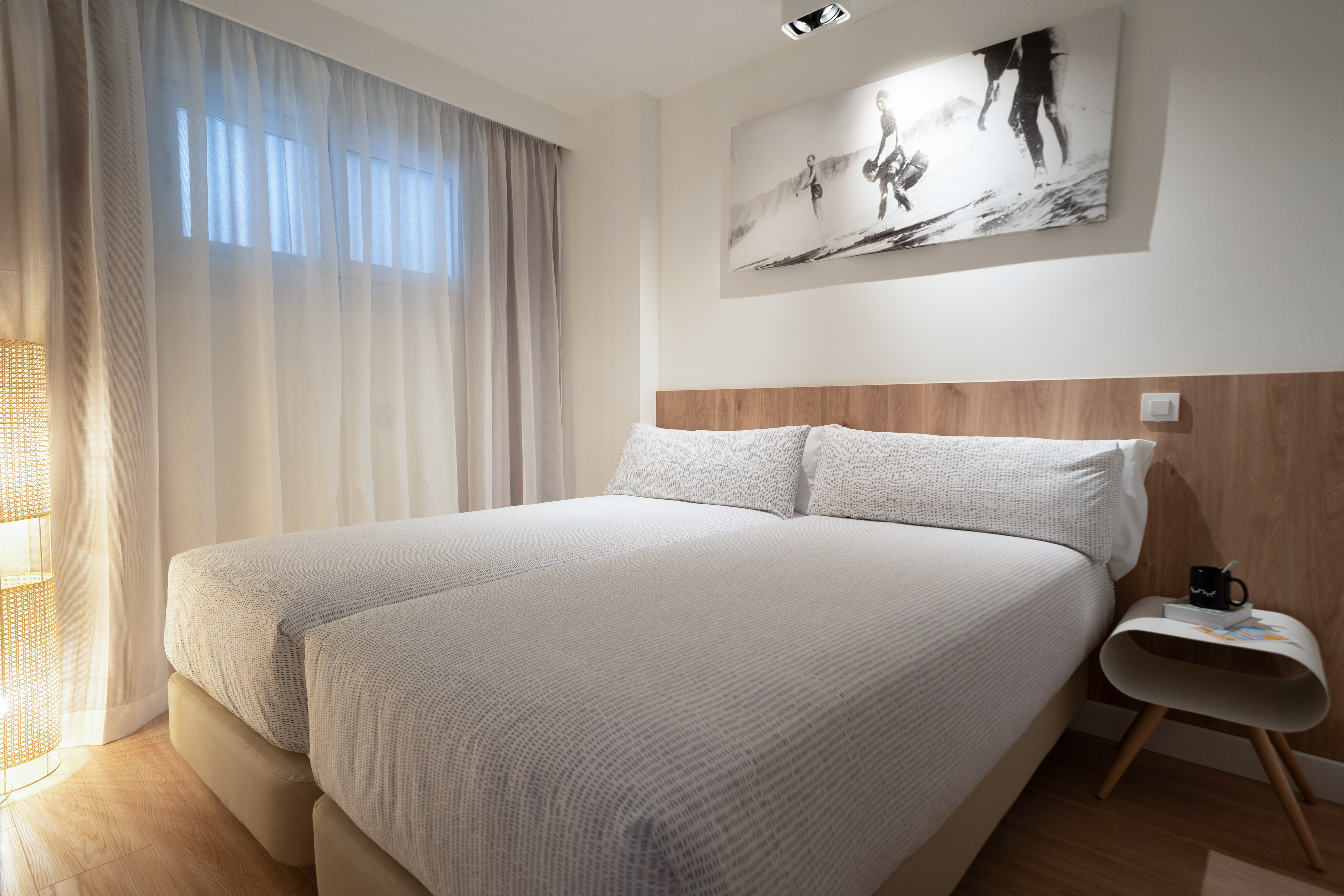 Modern bedroom with twin beds, wooden headboard, window, and surf art.