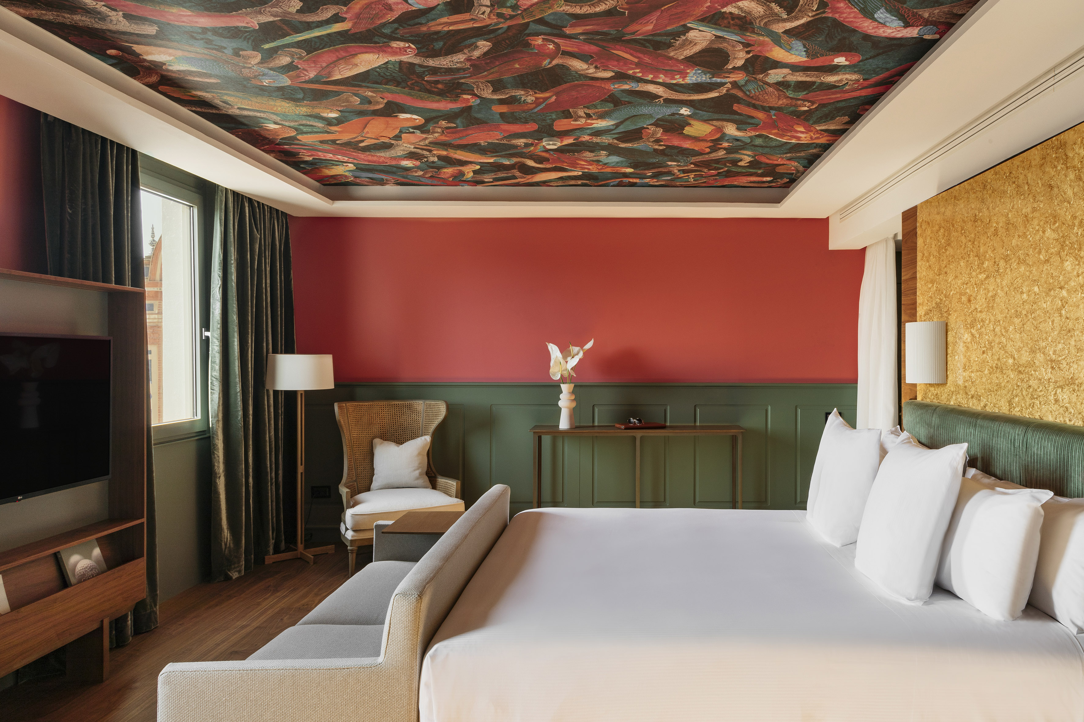 Luxury hotel bedroom with colorful bird ceiling, red walls, and modern furnishings.
