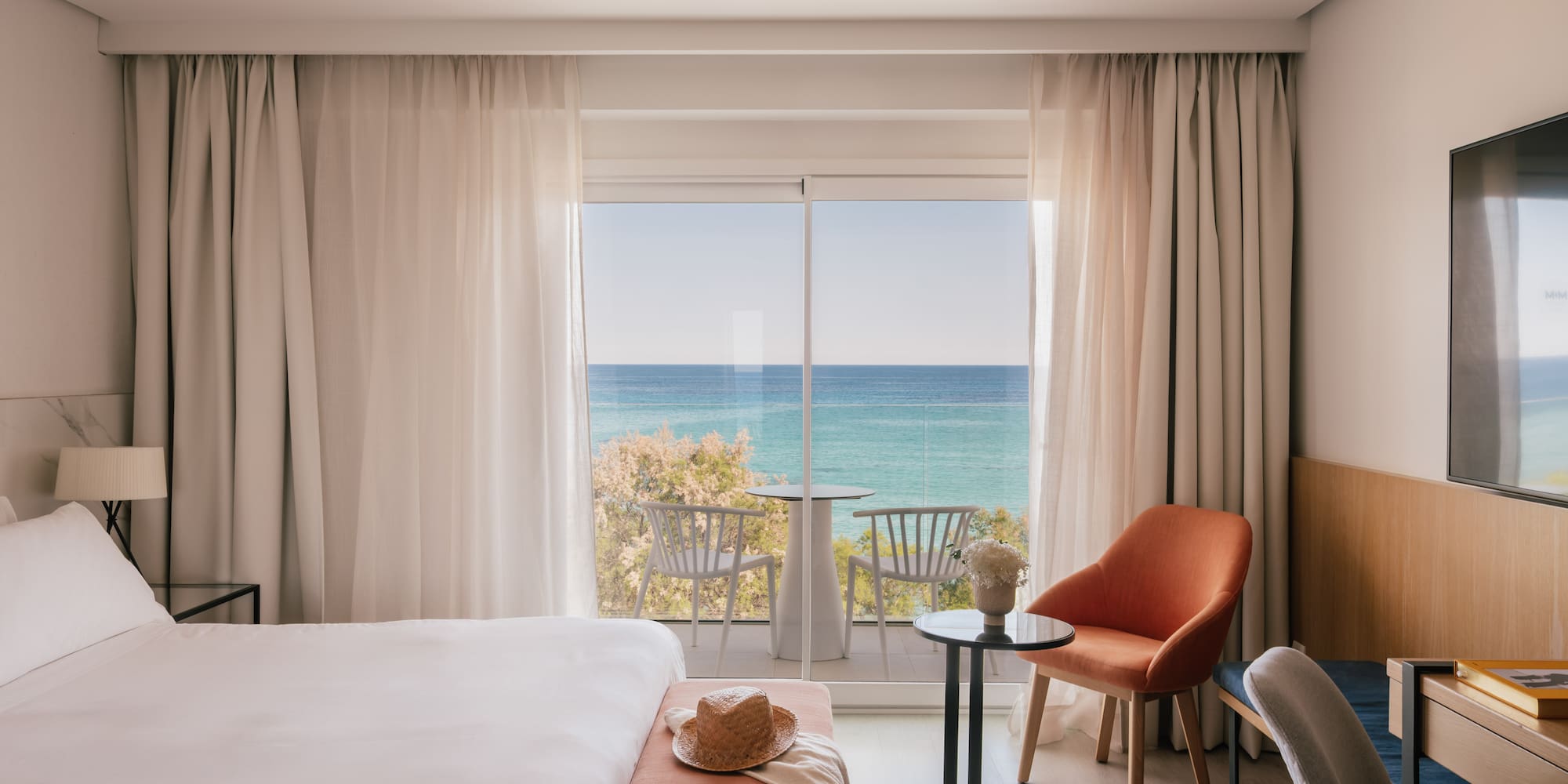 Habitación de hotel moderna con cama y balcón con vistas al mar y playa.