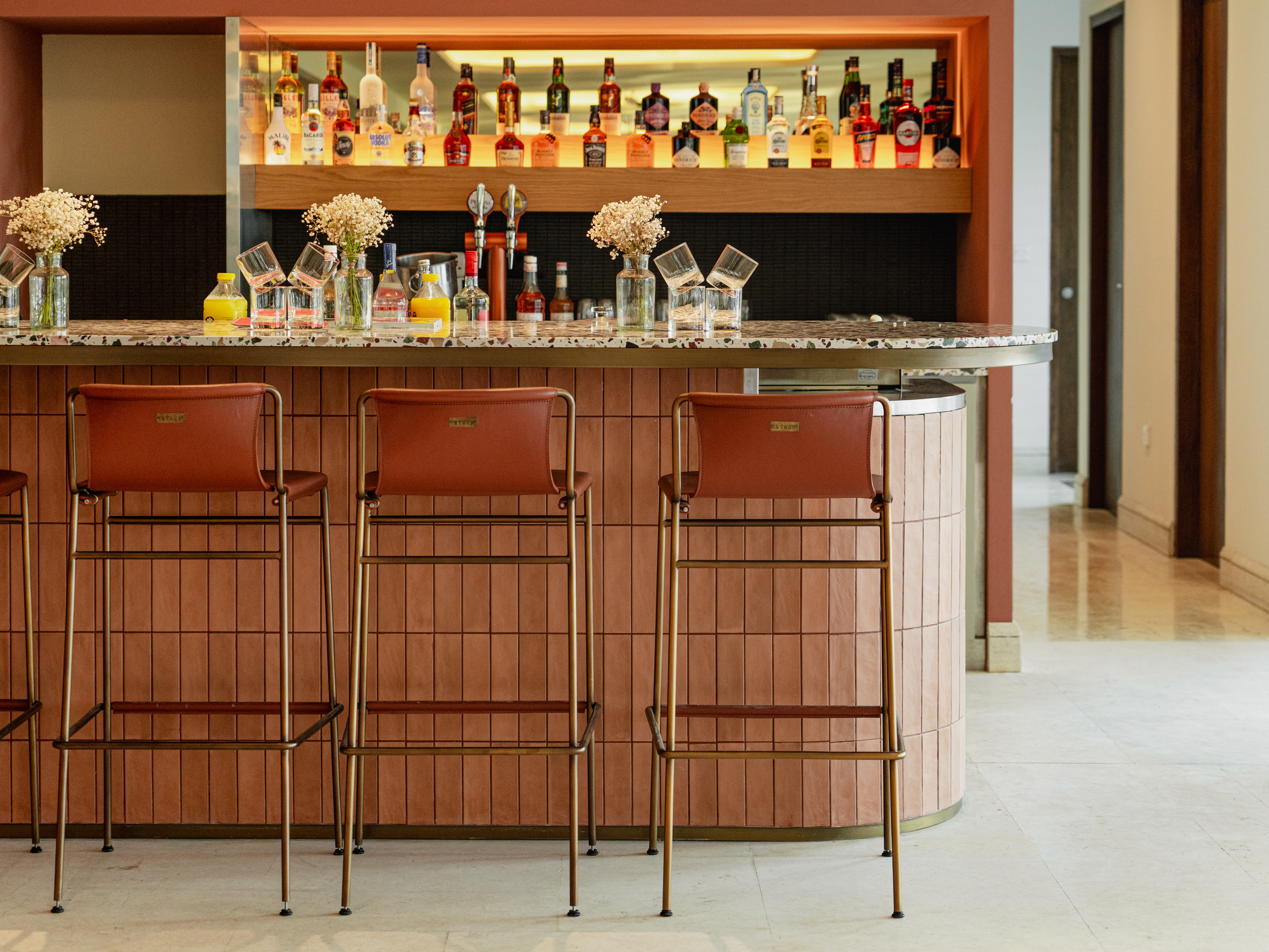 Modern bar with terrazzo counter, brown leather stools, and backlit liquor display.