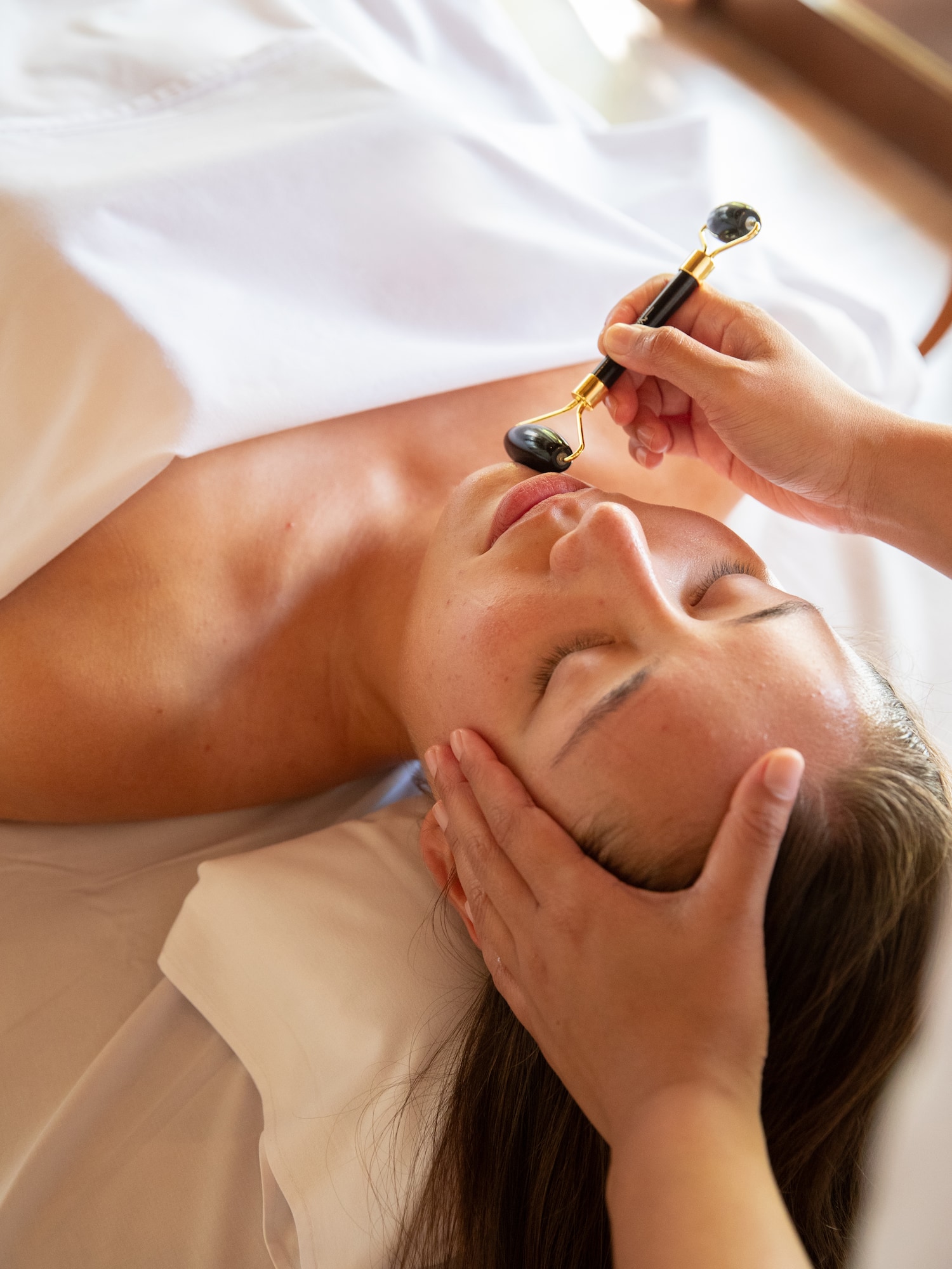 Relaxing facial massage with a dark stone roller on a woman's face.