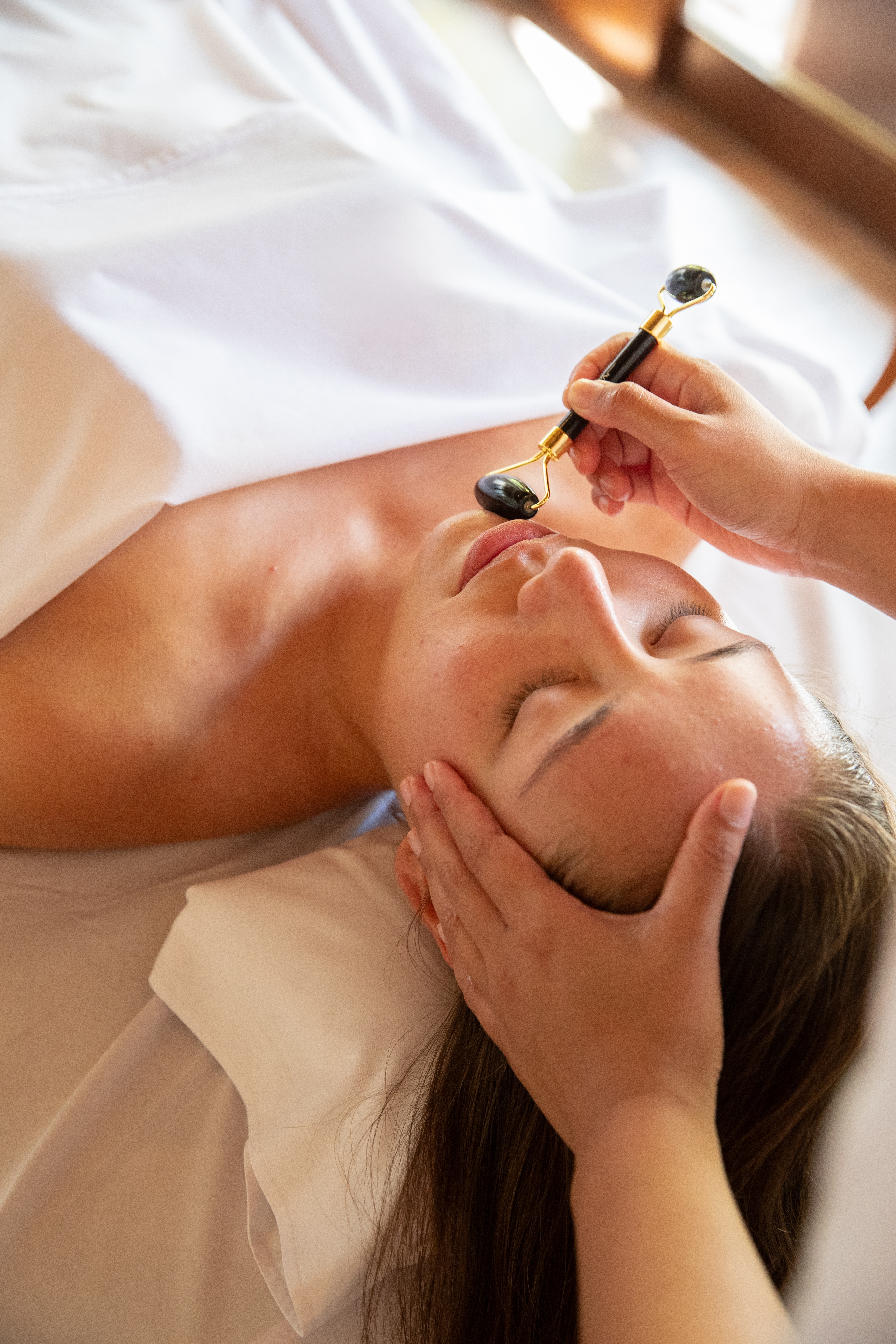 Relaxing facial massage with a dark stone roller on a woman's face.
