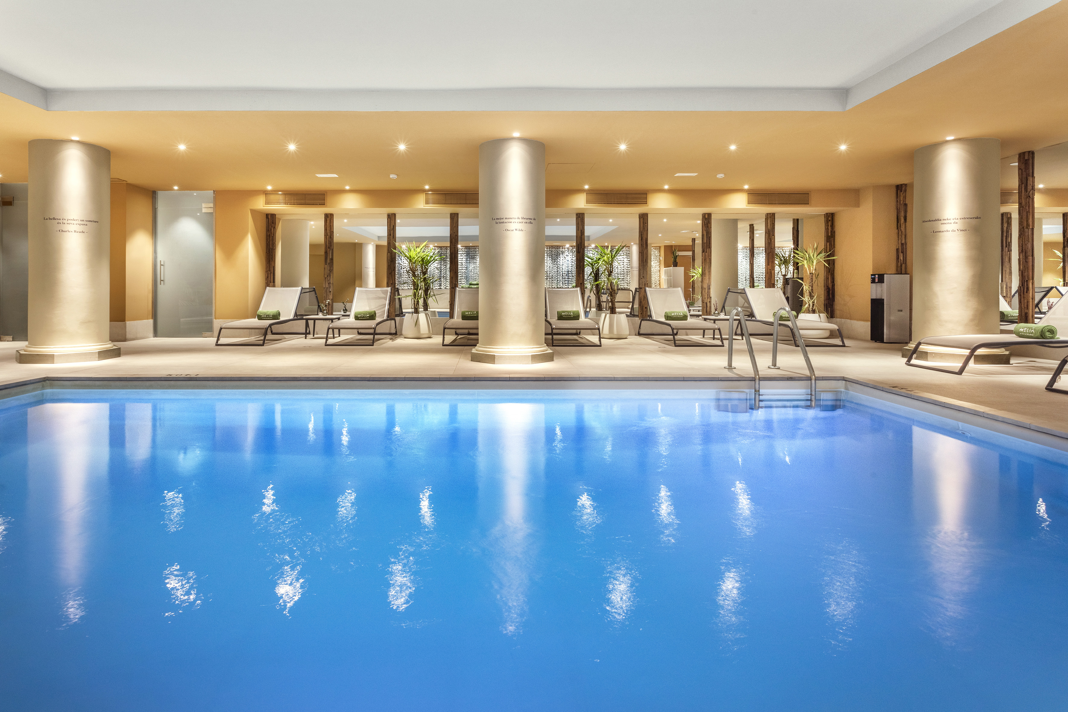 Modern indoor swimming pool, lounge chairs, warm lighting, luxury hotel spa.