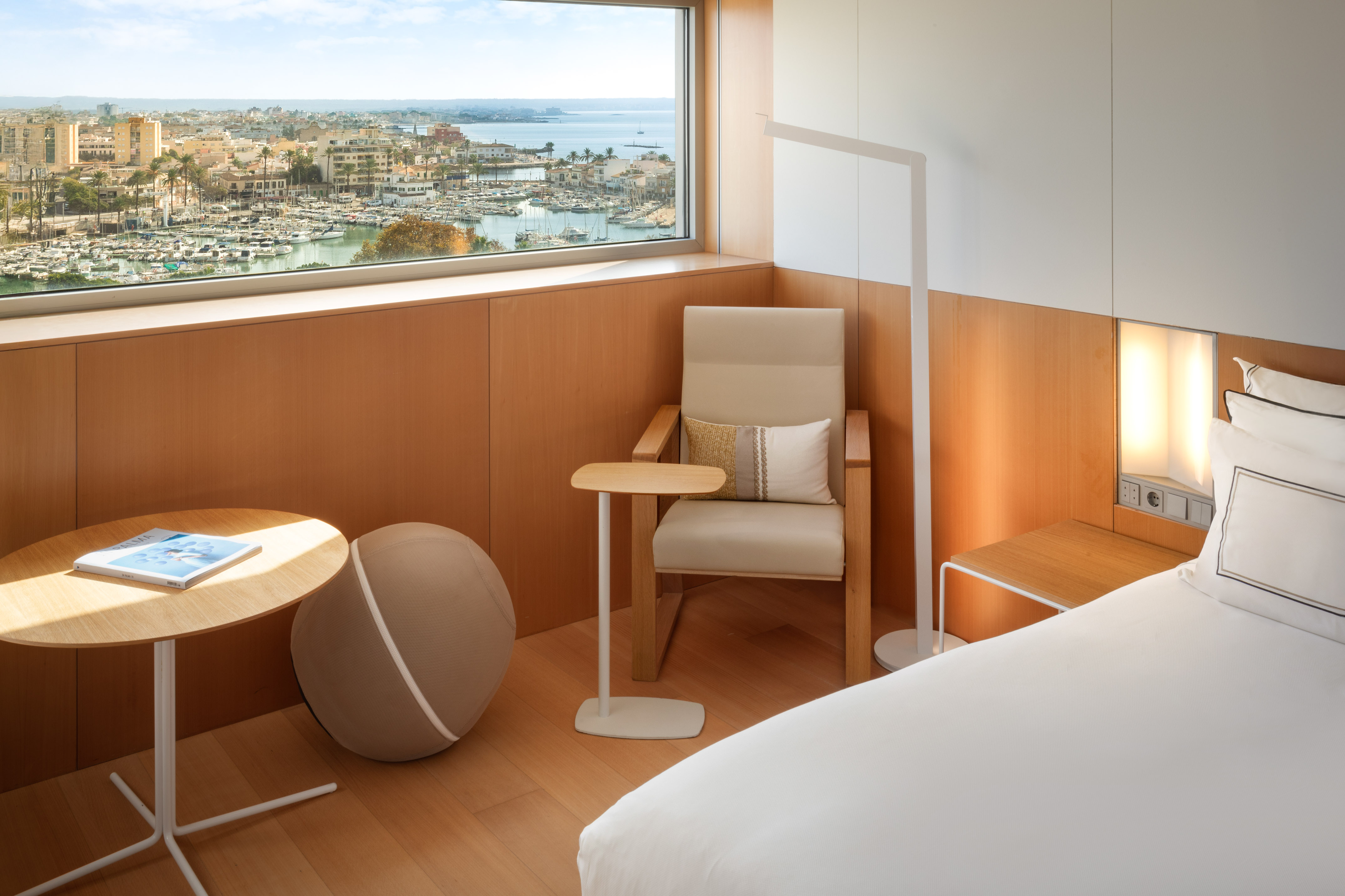 Modern hotel room with panoramic harbor city view, bed, and light wood interior.