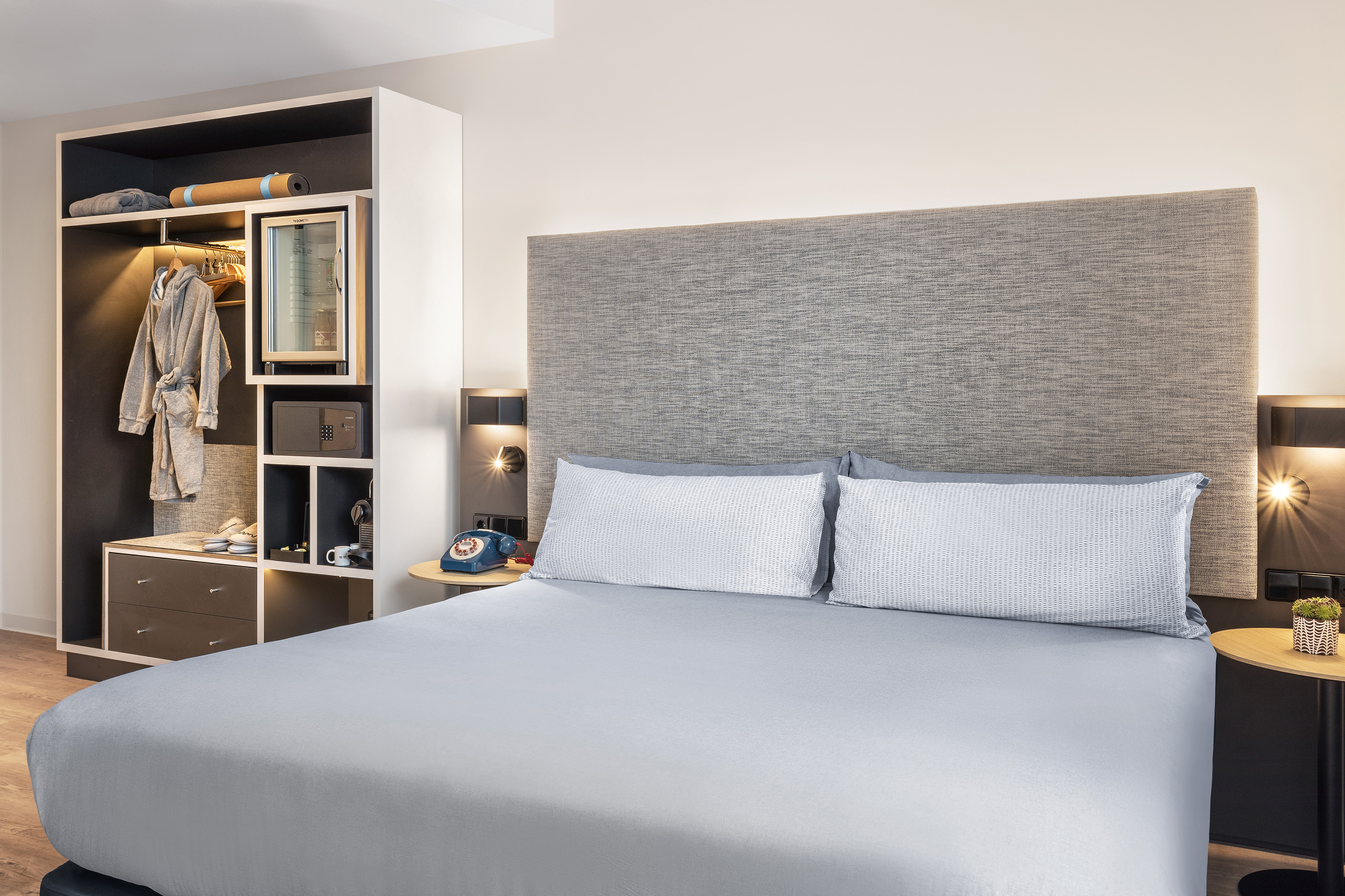 Cozy hotel room with grey bed, wardrobe, minibar, safe, and Nespresso.