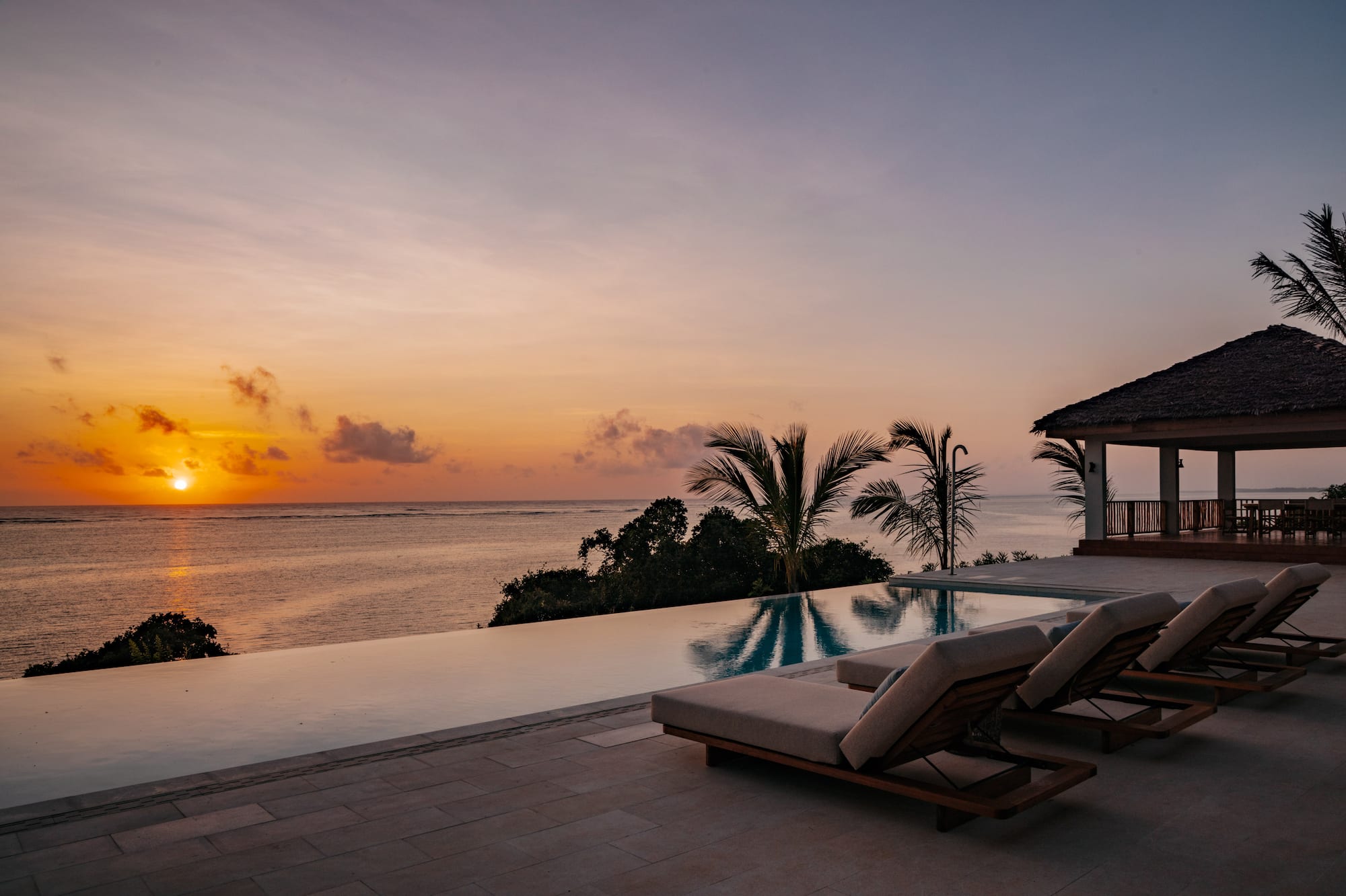 a pool with lounge chairs and a house overlooking the ocean
