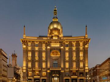 Assicurazioni Generali building in Milan, illuminated at dusk, with golden dome.
