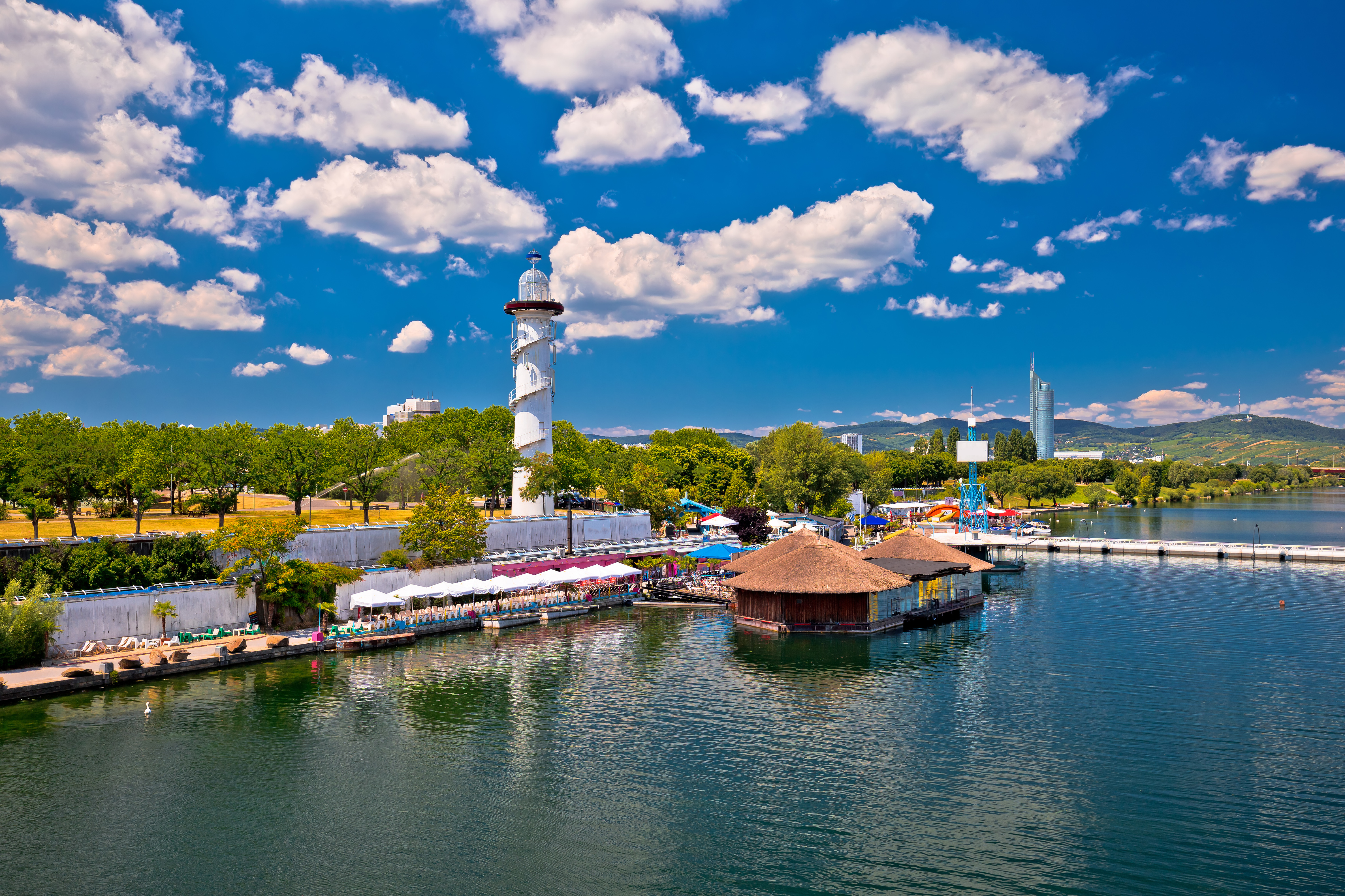 Vienna's Old Danube waterfront with lighthouse, restaurants, and modern skyscraper.