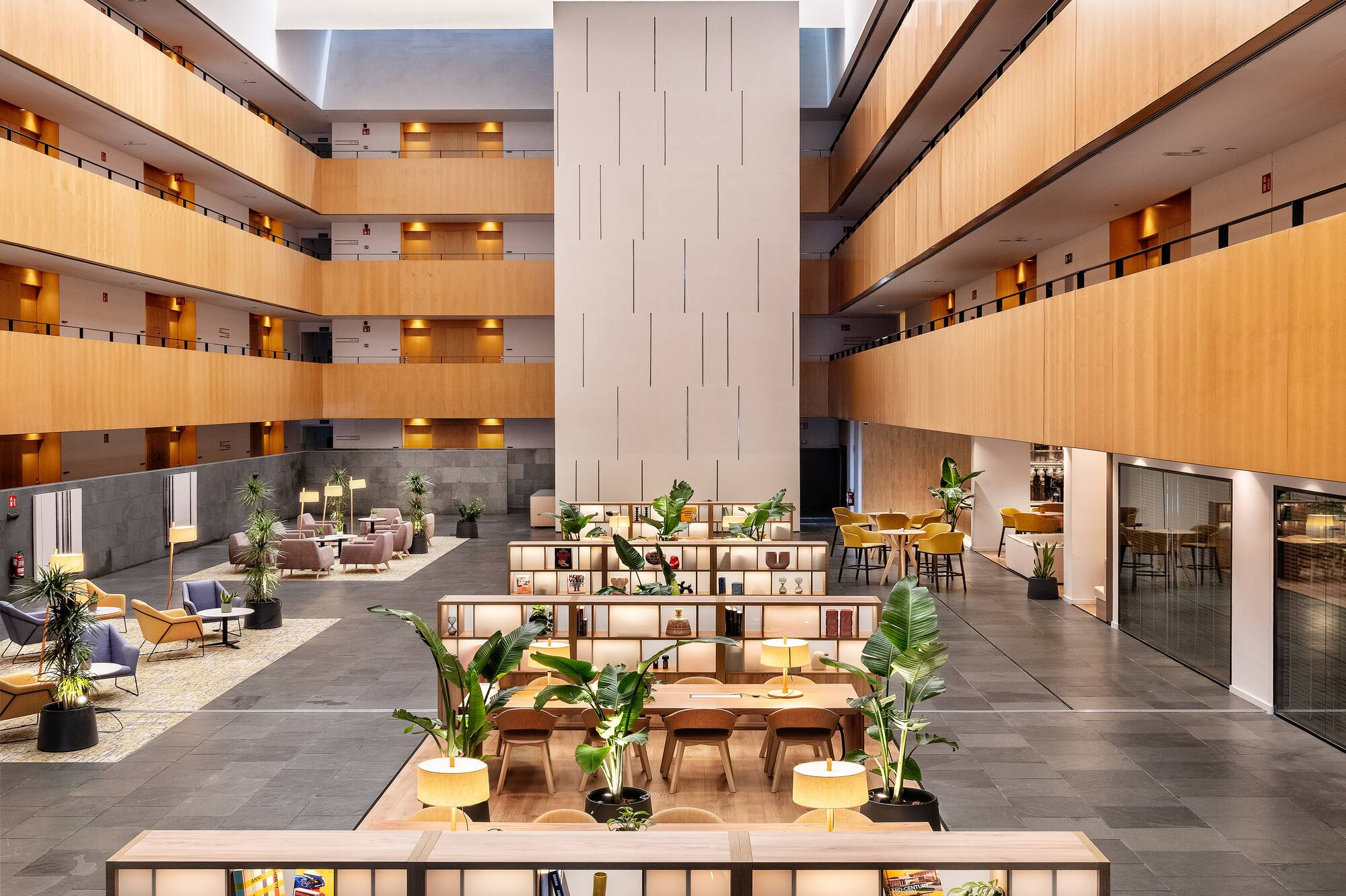 Modern hotel atrium with wood levels, lounge seating, and interior plants.