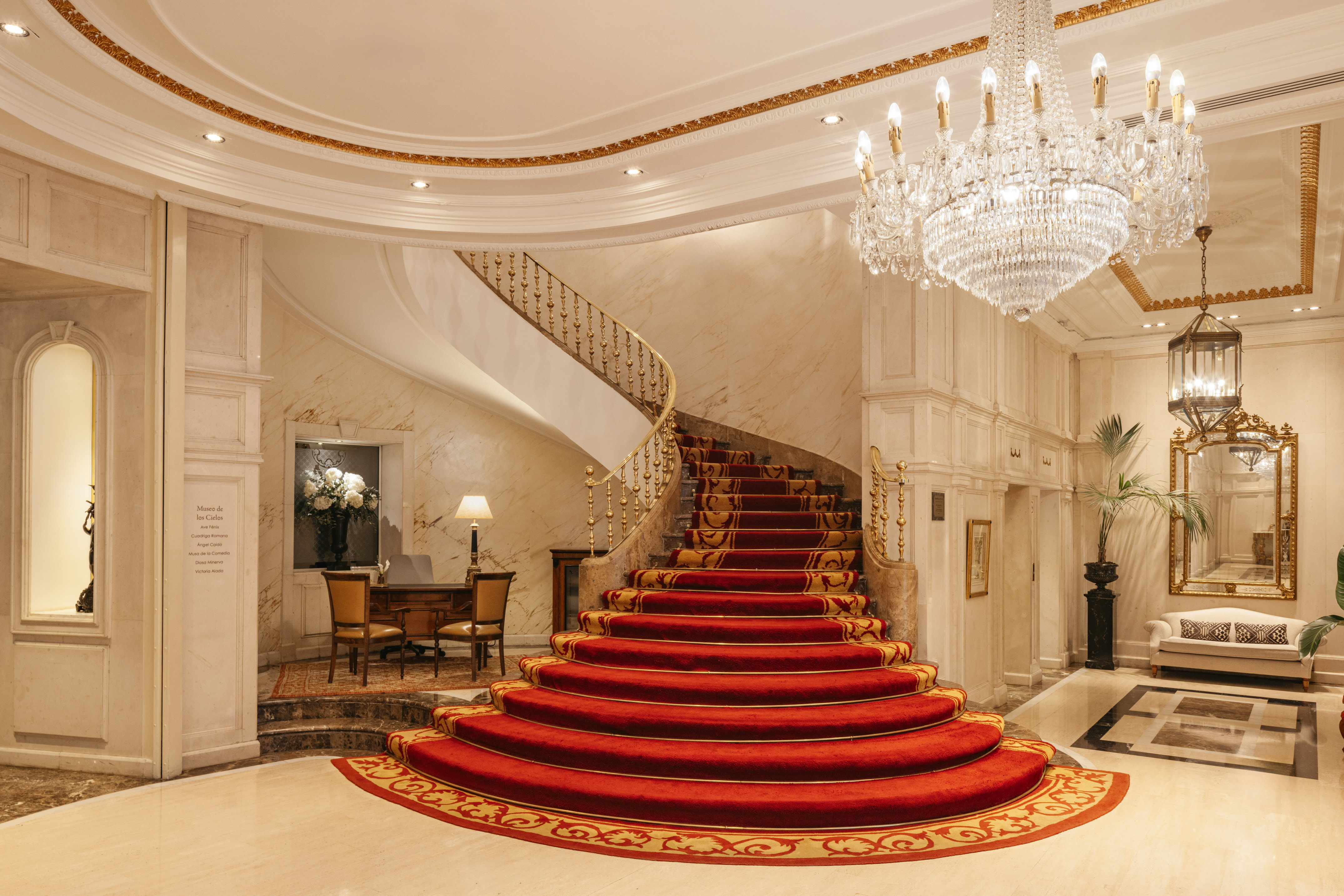 Grand red carpet spiral staircase in a luxurious hotel lobby with chandelier.