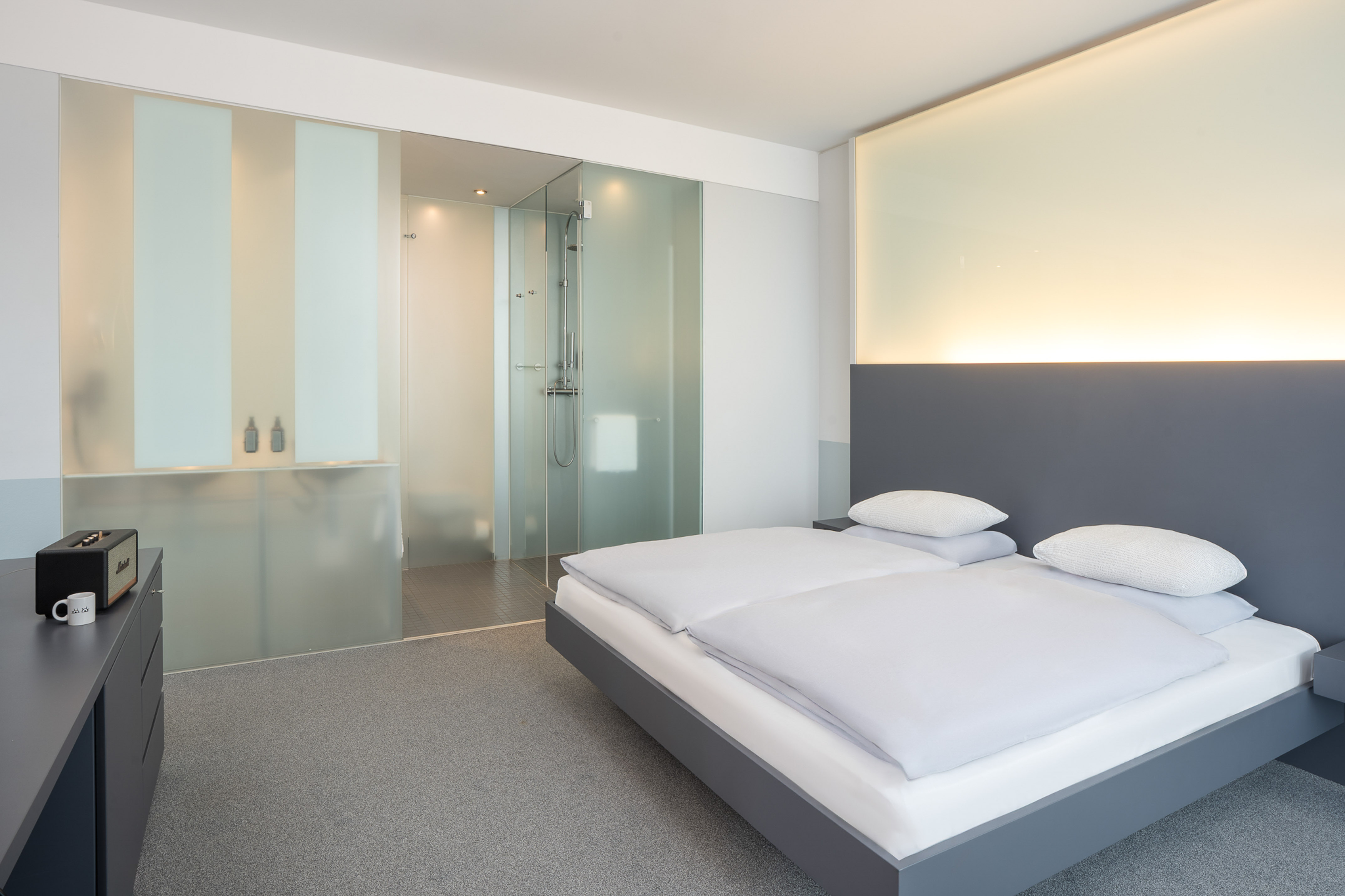 Modern hotel room with bed, grey headboard, and frosted glass shower.