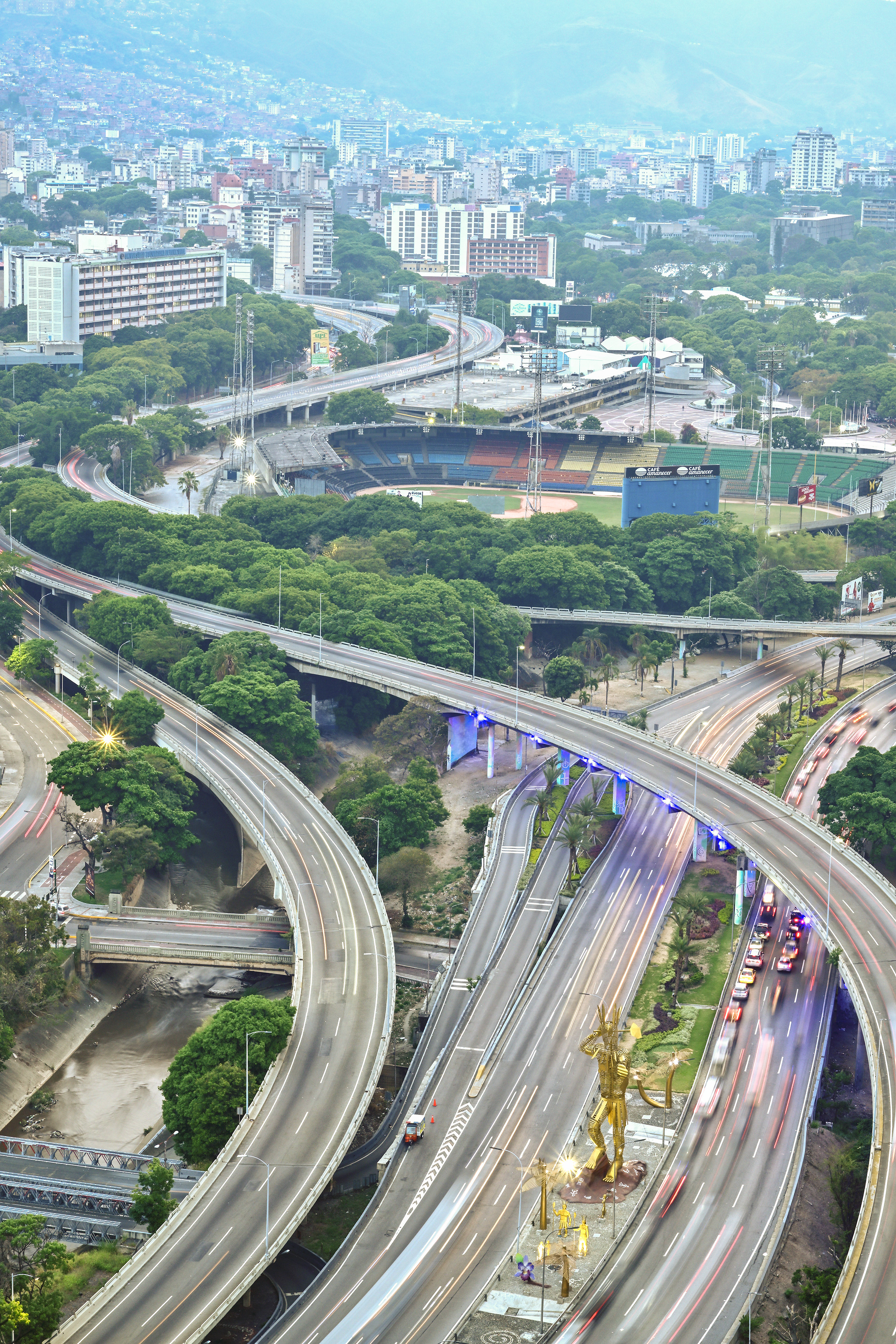 Caracas highway interchange, traffic trails, golden warrior statue, stadium.