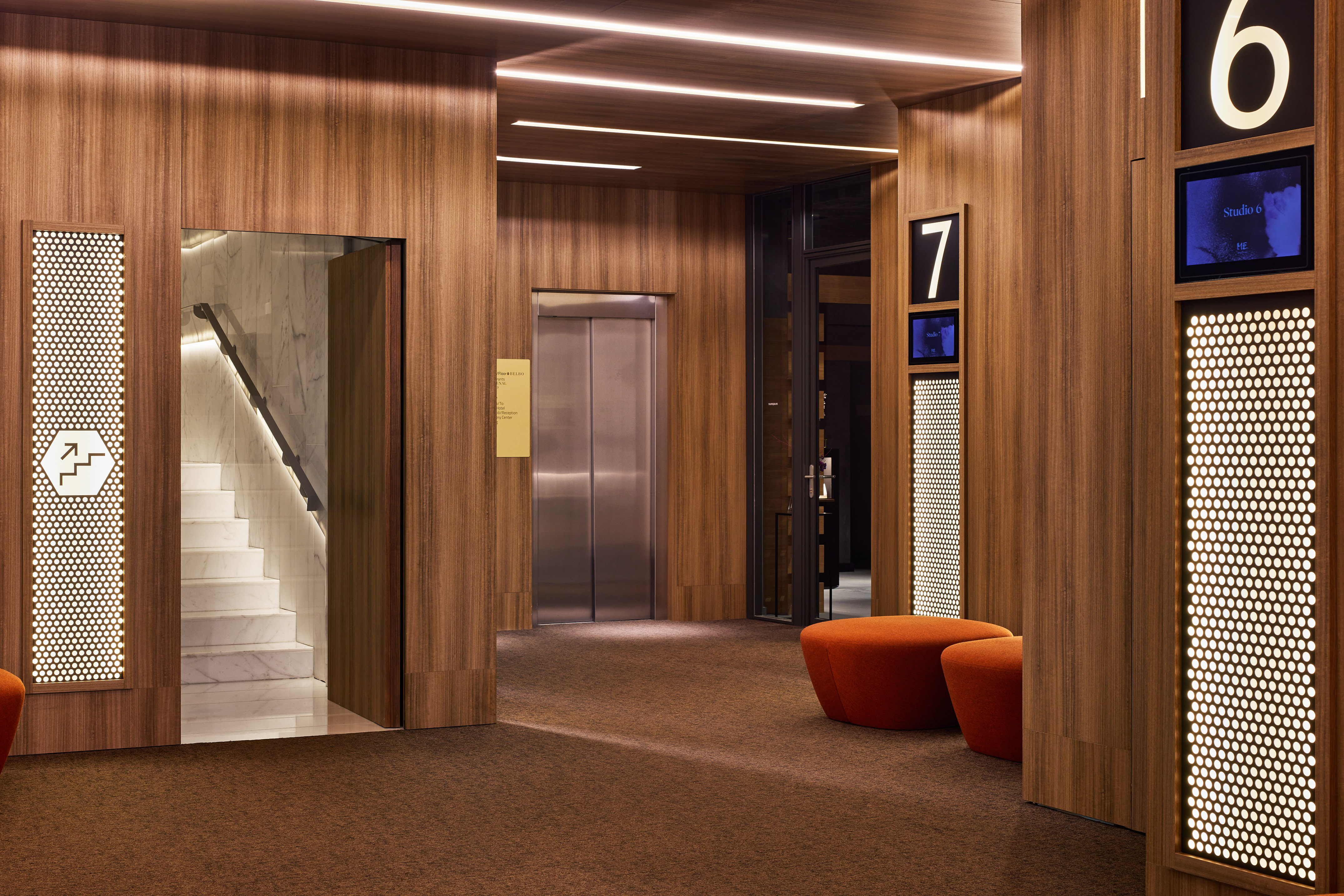 Modern wood-paneled hallway with elevator, marble stairs, and studio wayfinding.