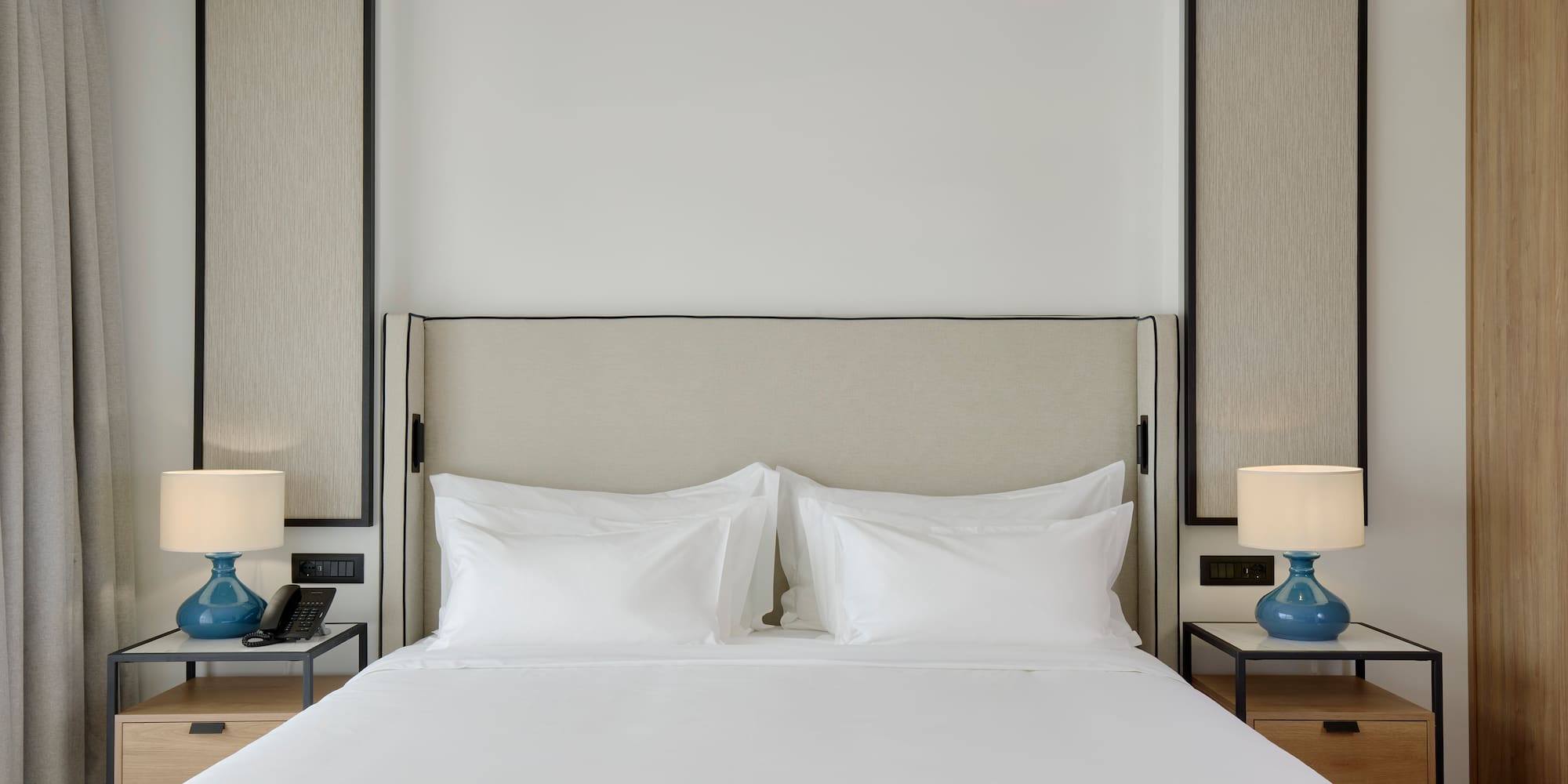 a bed with white sheets and a blue lamp on a table