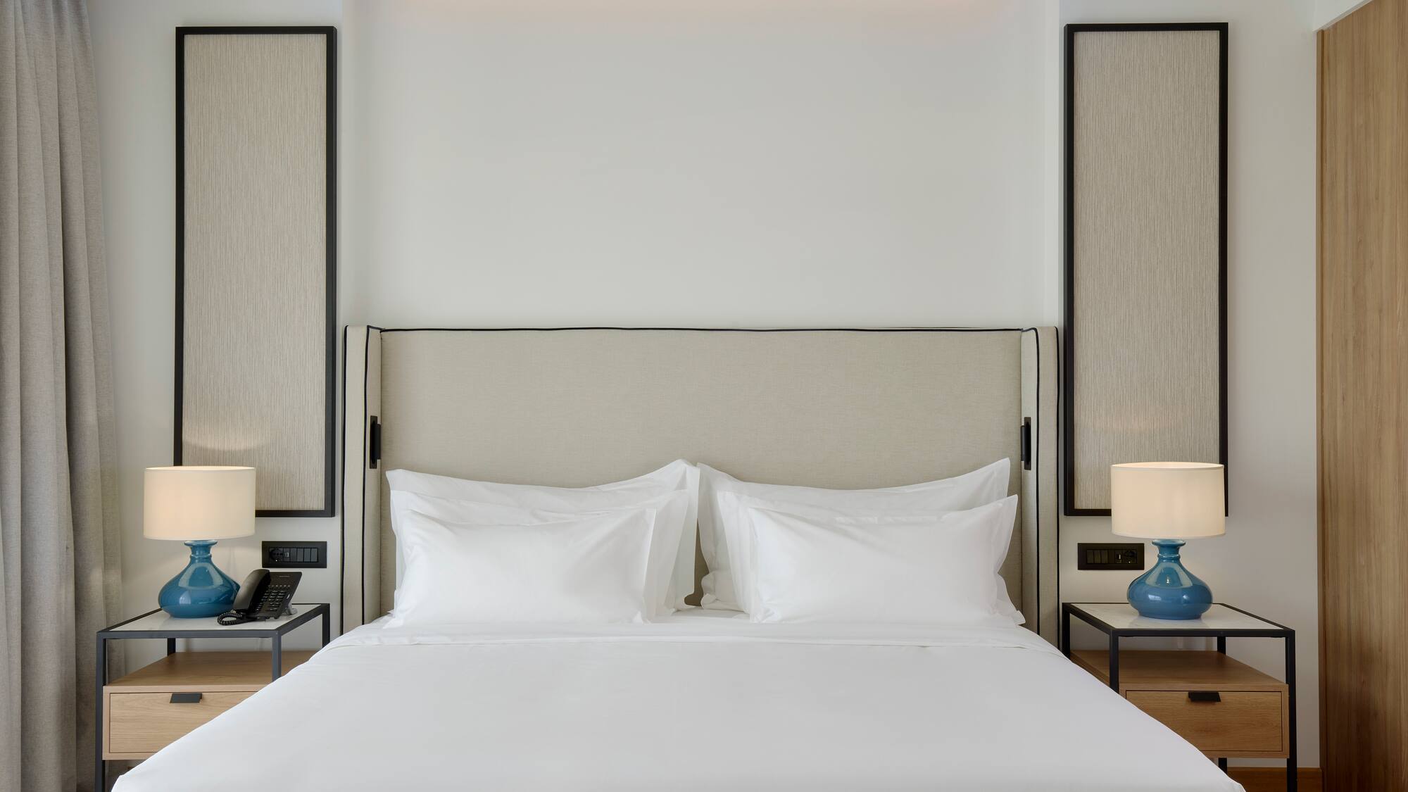 a bed with white sheets and a blue lamp on a table