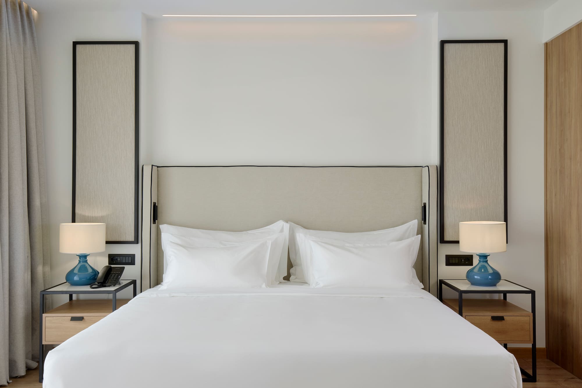 a bed with white sheets and a blue lamp on a table