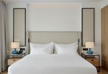 a bed with white sheets and a blue lamp on a table